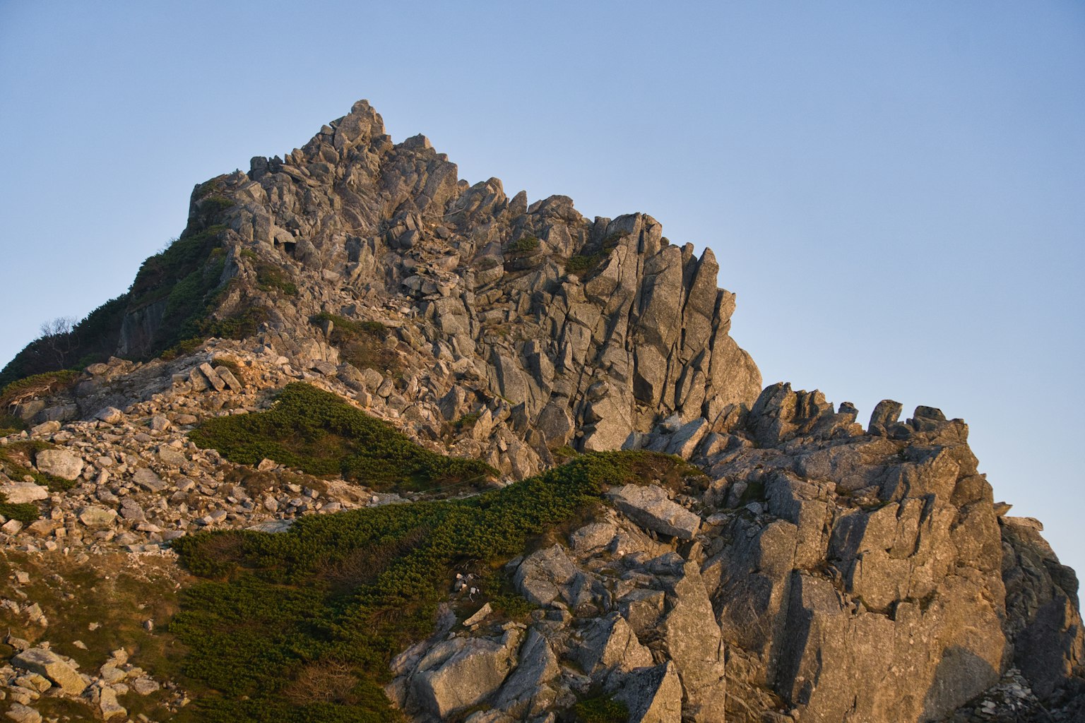 Rocky mountain landscape with sharp peaks and greenery under a clear sky