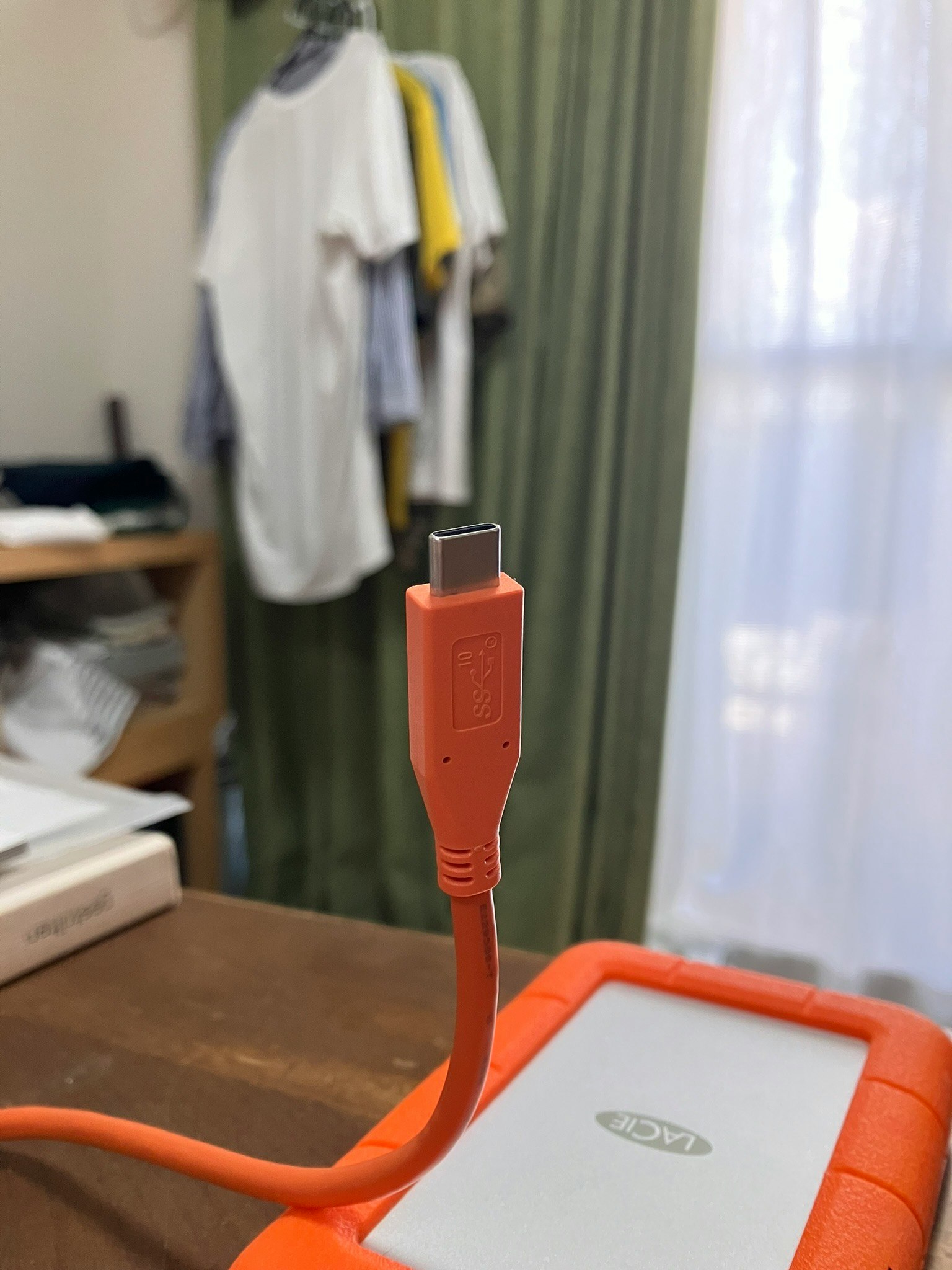 Un cable USB naranja en primer plano con camisetas y cortinas de fondo