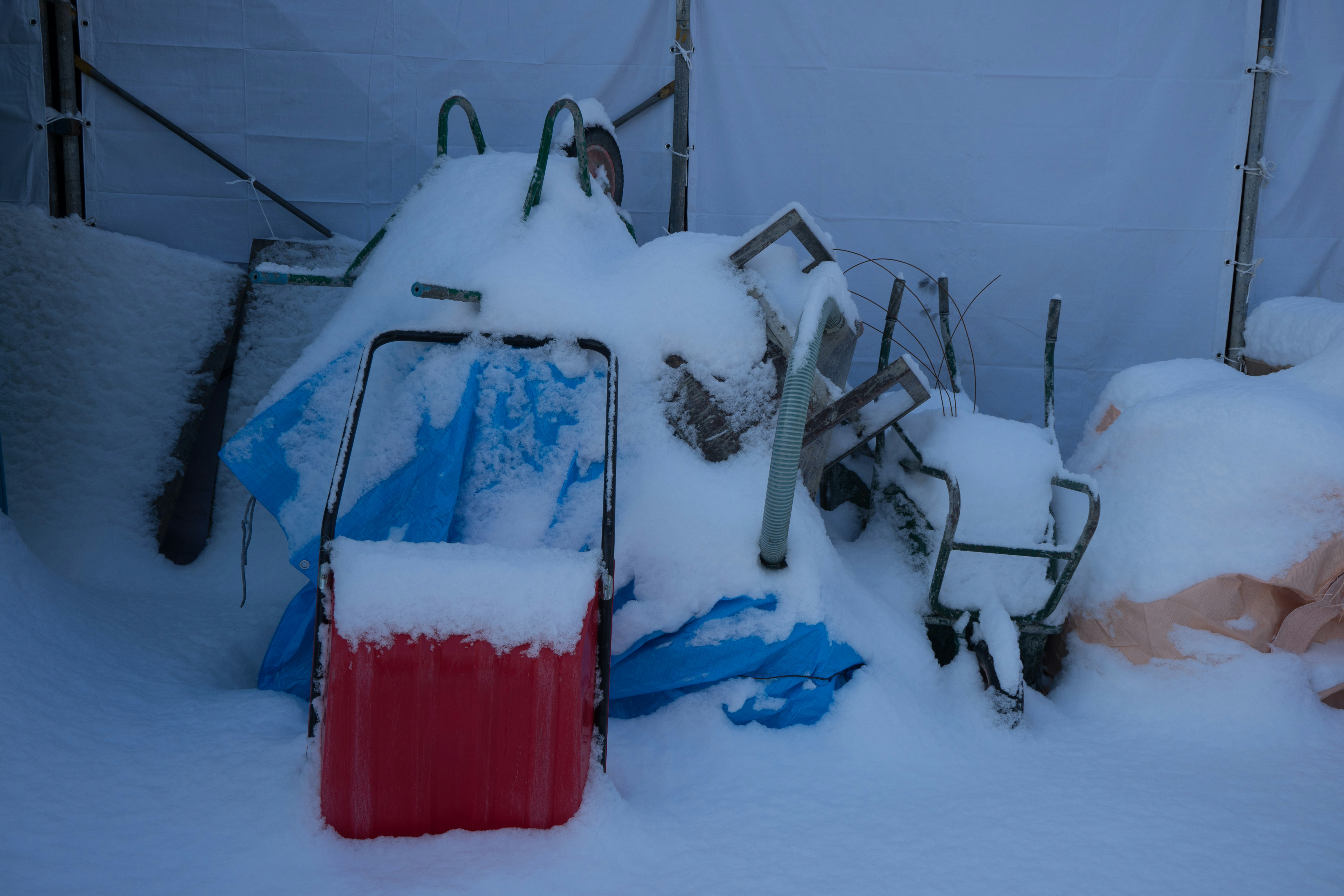 Snow-covered outdoor shed tools and wheelbarrow in a yard