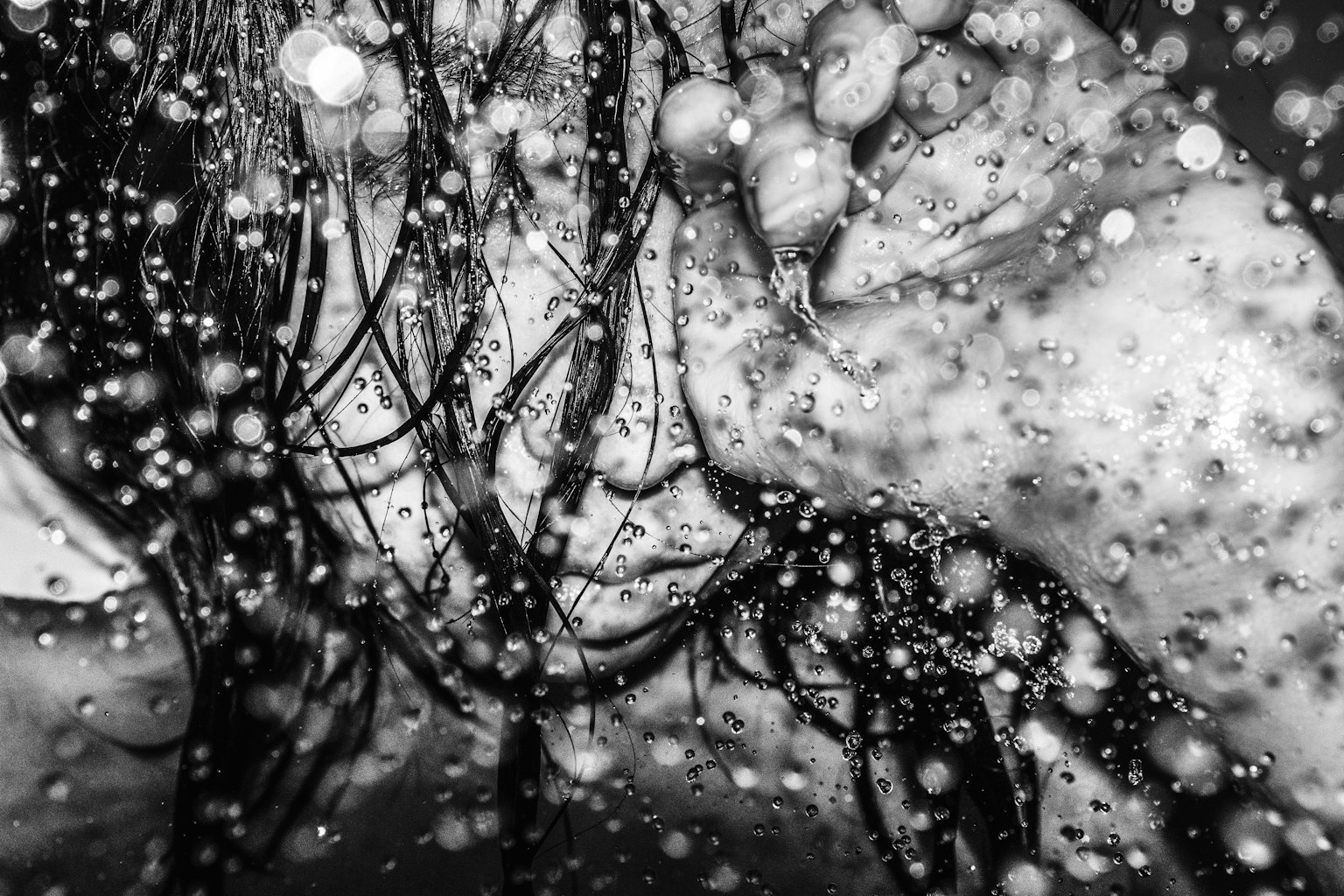 Image en noir et blanc d'un visage et de cheveux immergés dans des éclaboussures d'eau