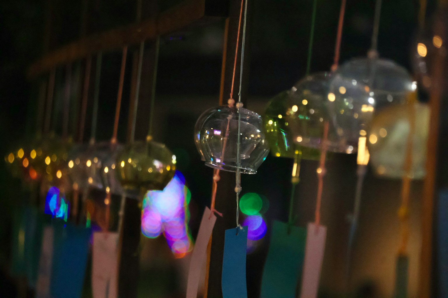 ระฆังลมหลากสีแขวนอยู่ในฉากกลางคืน การตกแต่งที่ส่องสว่างอยู่เบื้องหลัง