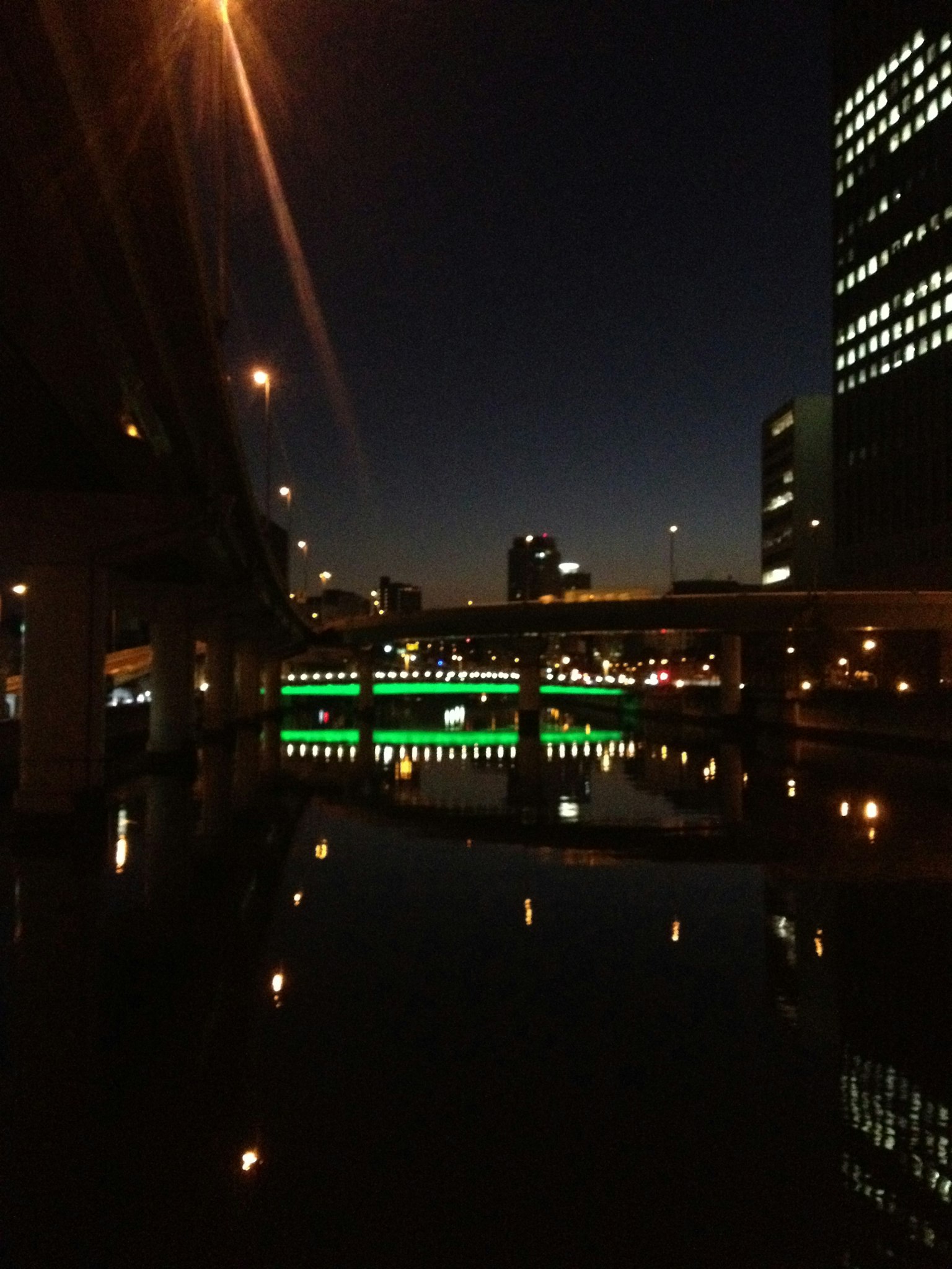 Paesaggio urbano notturno con ponte illuminato e edifici che si riflettono nell'acqua
