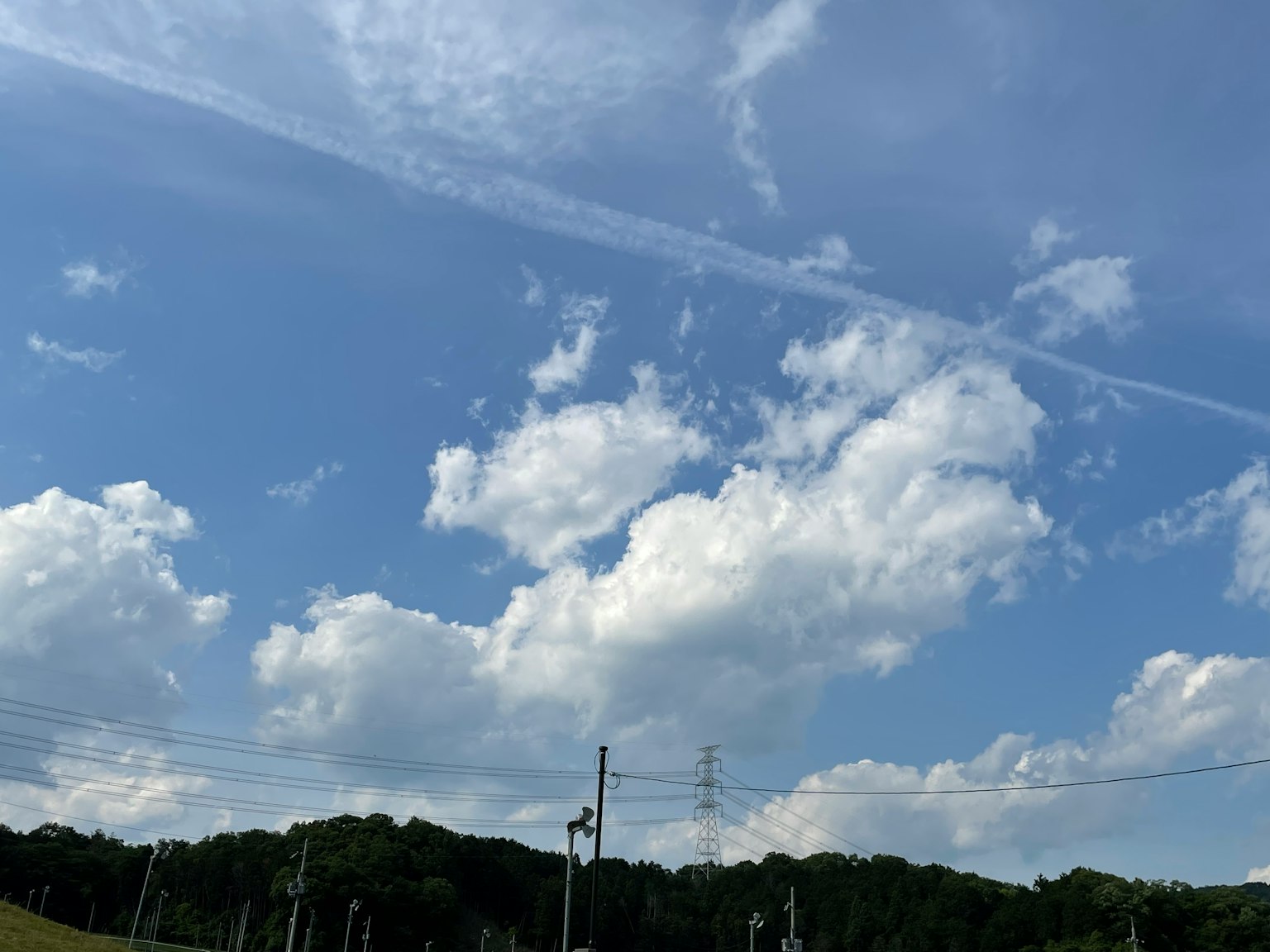 Un paisaje con cielo azul nubes blancas colinas verdes y postes eléctricos
