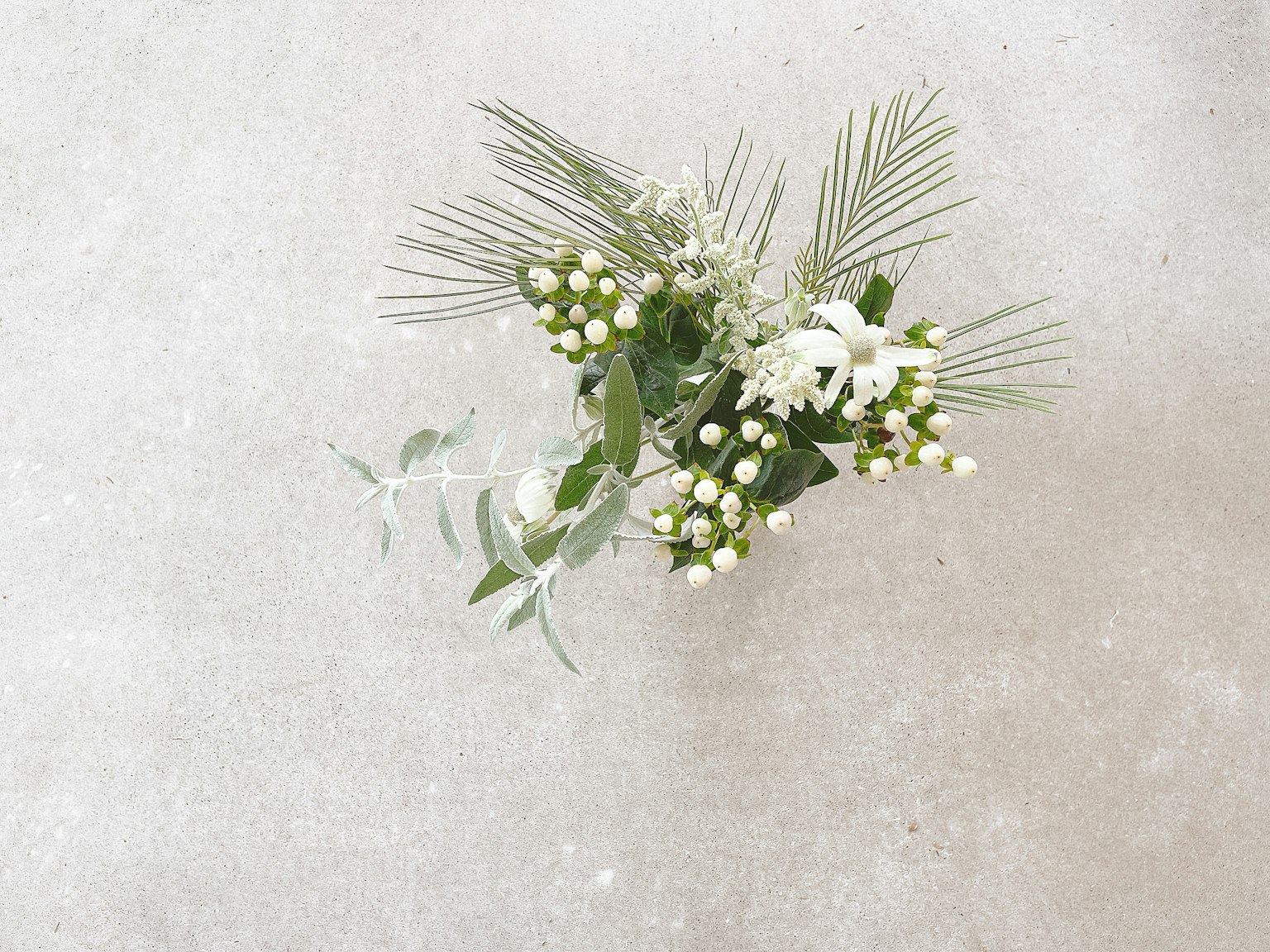 Un bellissimo bouquet di fiori bianchi e foglie verdi disposto su uno sfondo grigio
