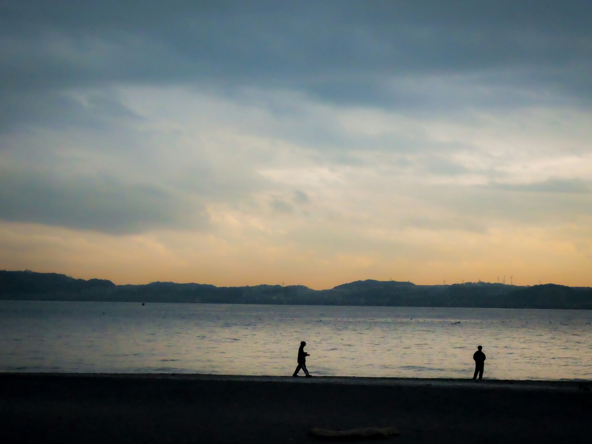夕暮れの湖畔を歩く人々のシルエット