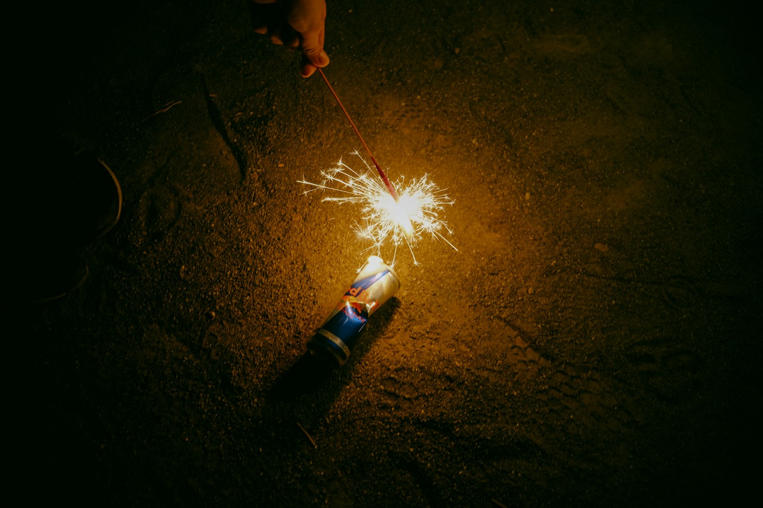 A hand holding a sparkler creating sparks on a sandy beach at night