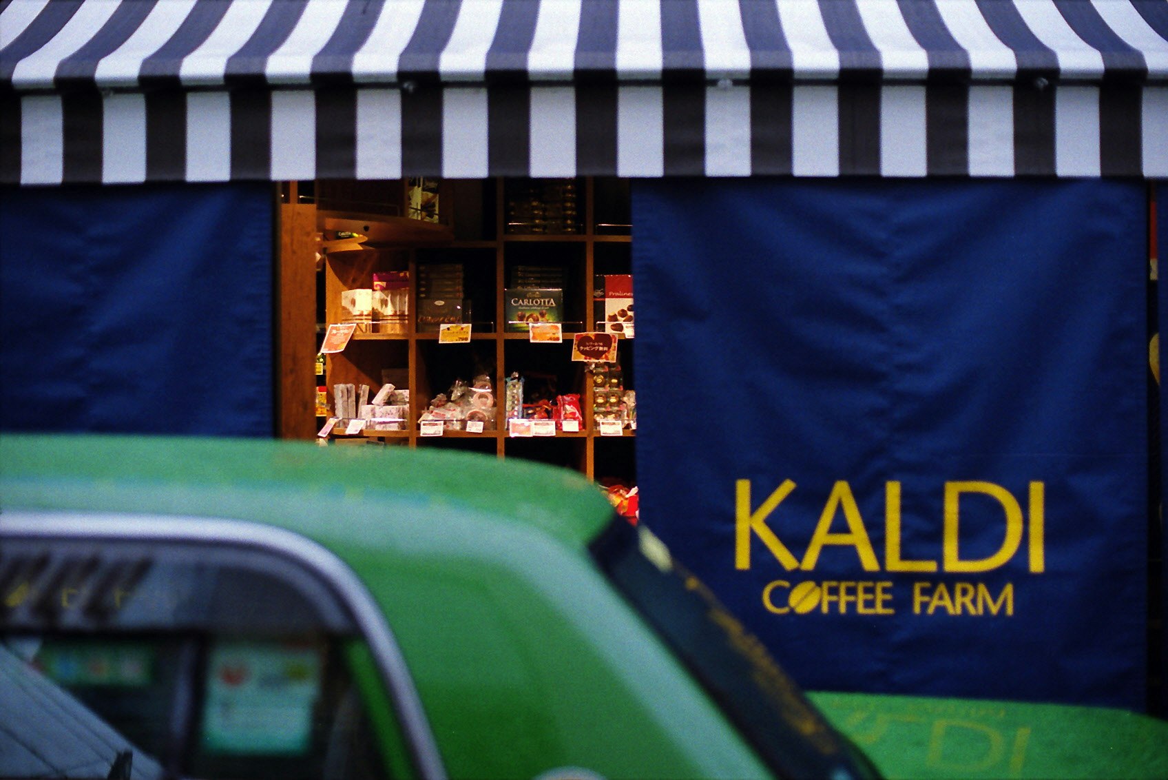 storefront sign with “KALDI COFFEE FARM” on a blue awning and a parked car