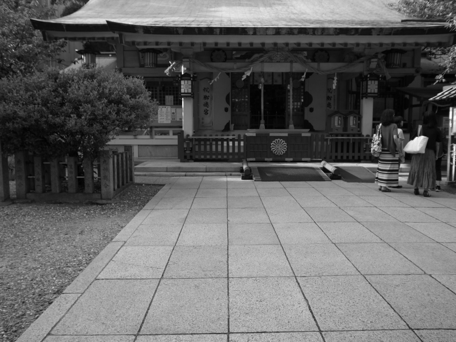 Imagen en blanco y negro de la entrada de un santuario con personas caminando en el patio