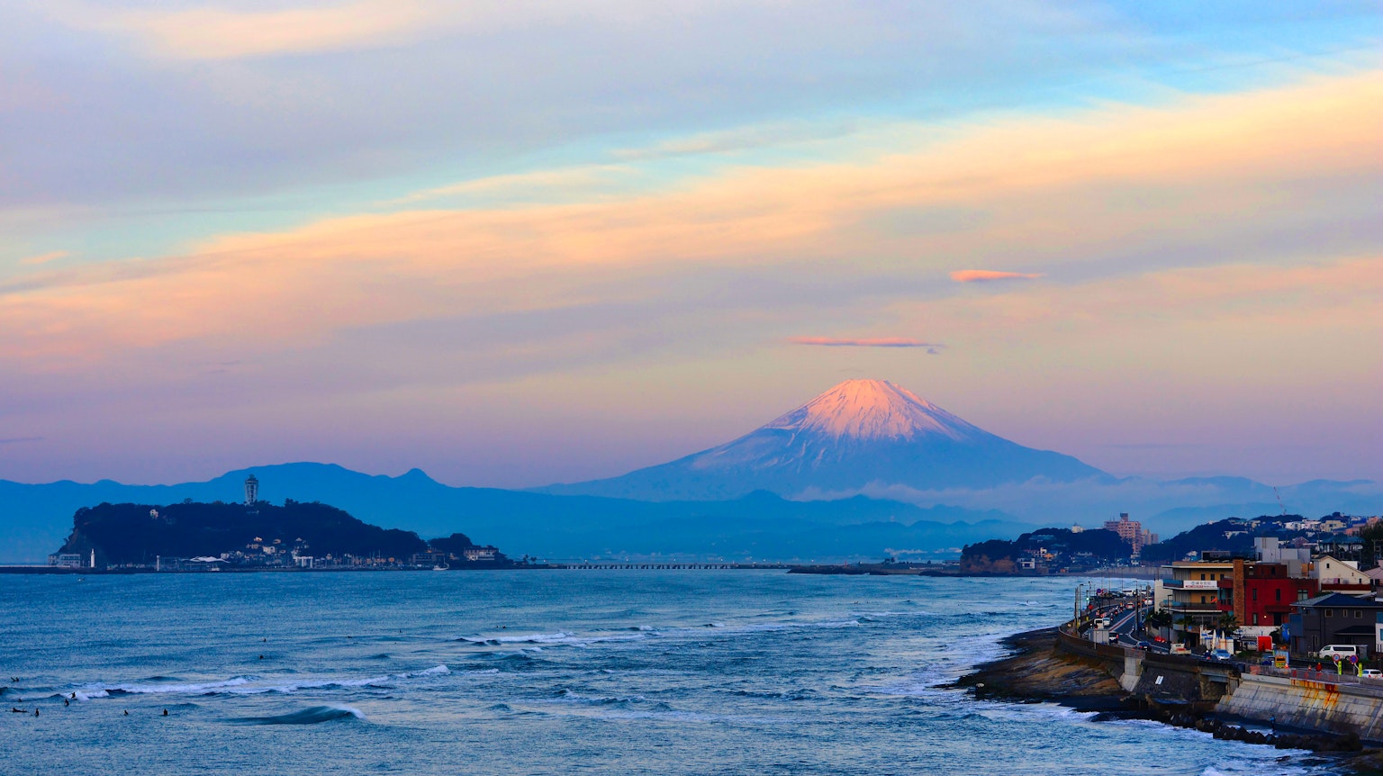 Küstenlandschaft mit dem Fuji im Hintergrund bunter Sonnenuntergangshimmel und sanfte Meereswellen
