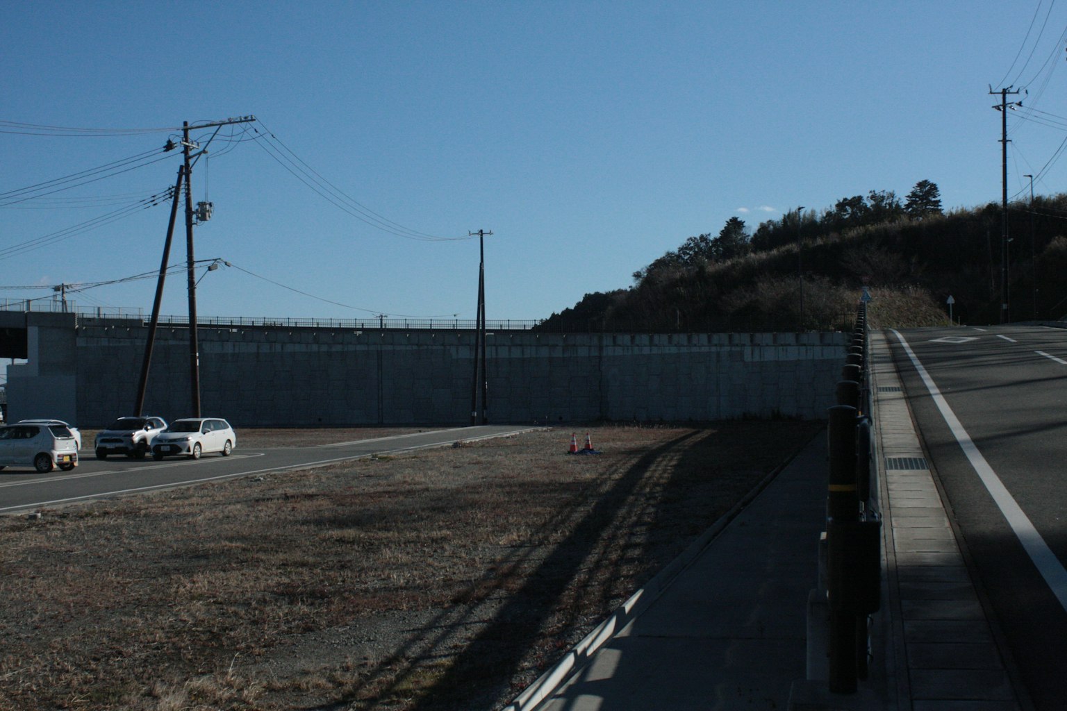 Vista di un alto muro di cemento accanto a una strada con pali elettrici