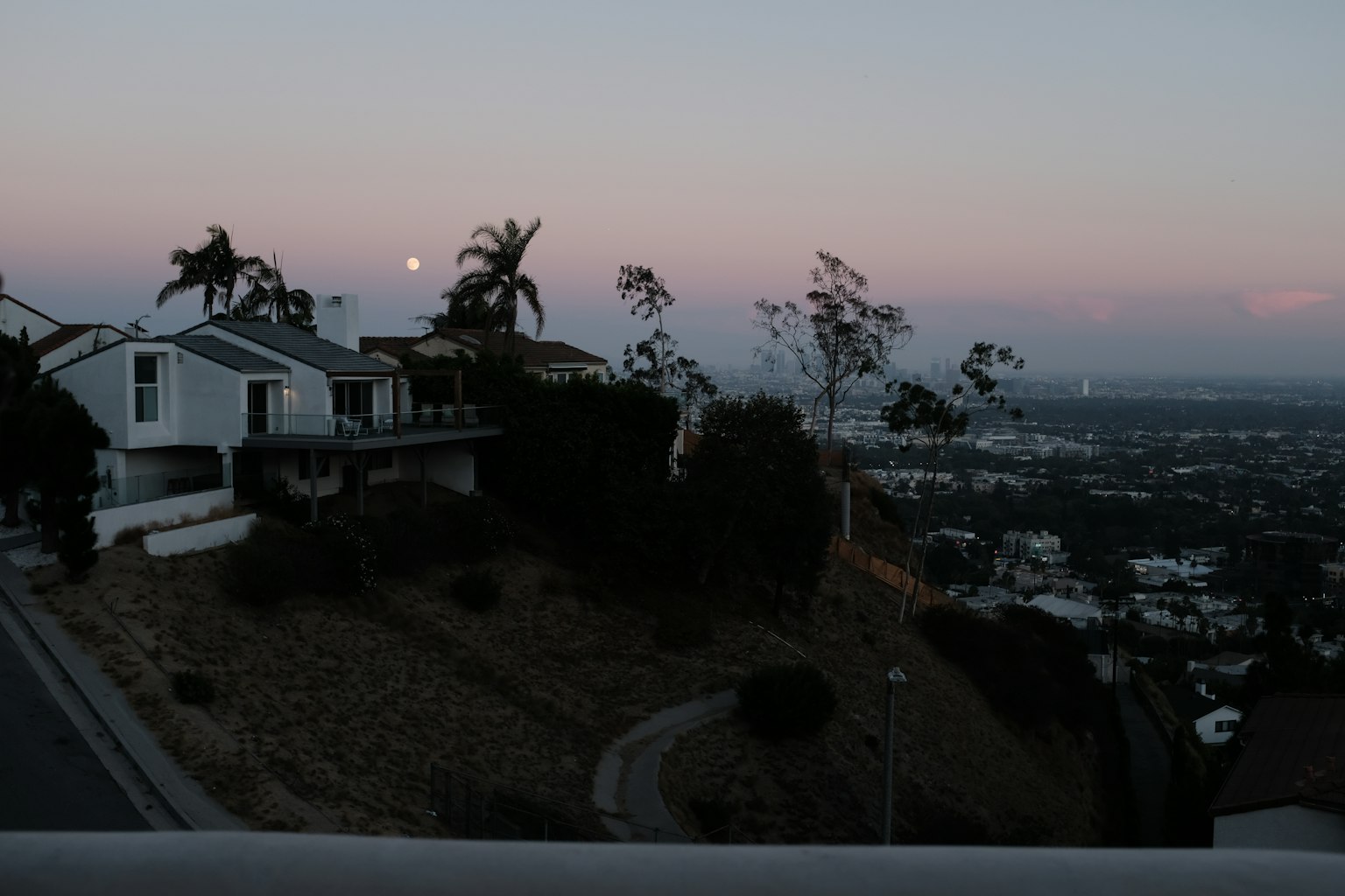Pemandangan rumah di bukit saat senja dengan bulan terlihat
