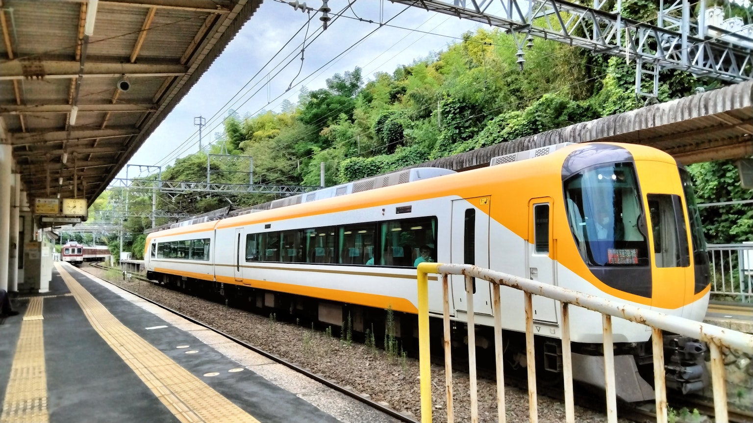 รถไฟสีเหลืองและขาวจอดอยู่ที่สถานีเงียบๆ พร้อมพื้นหลังสีเขียว