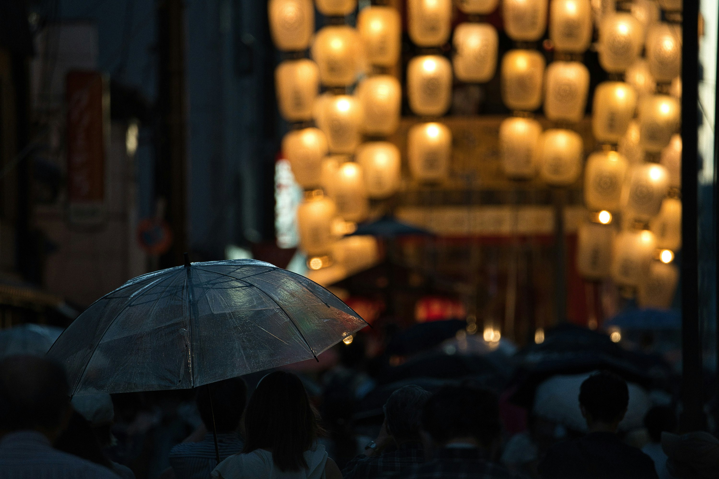 祇園祭の提灯が並ぶ雨の街で傘をさす人々の風景
