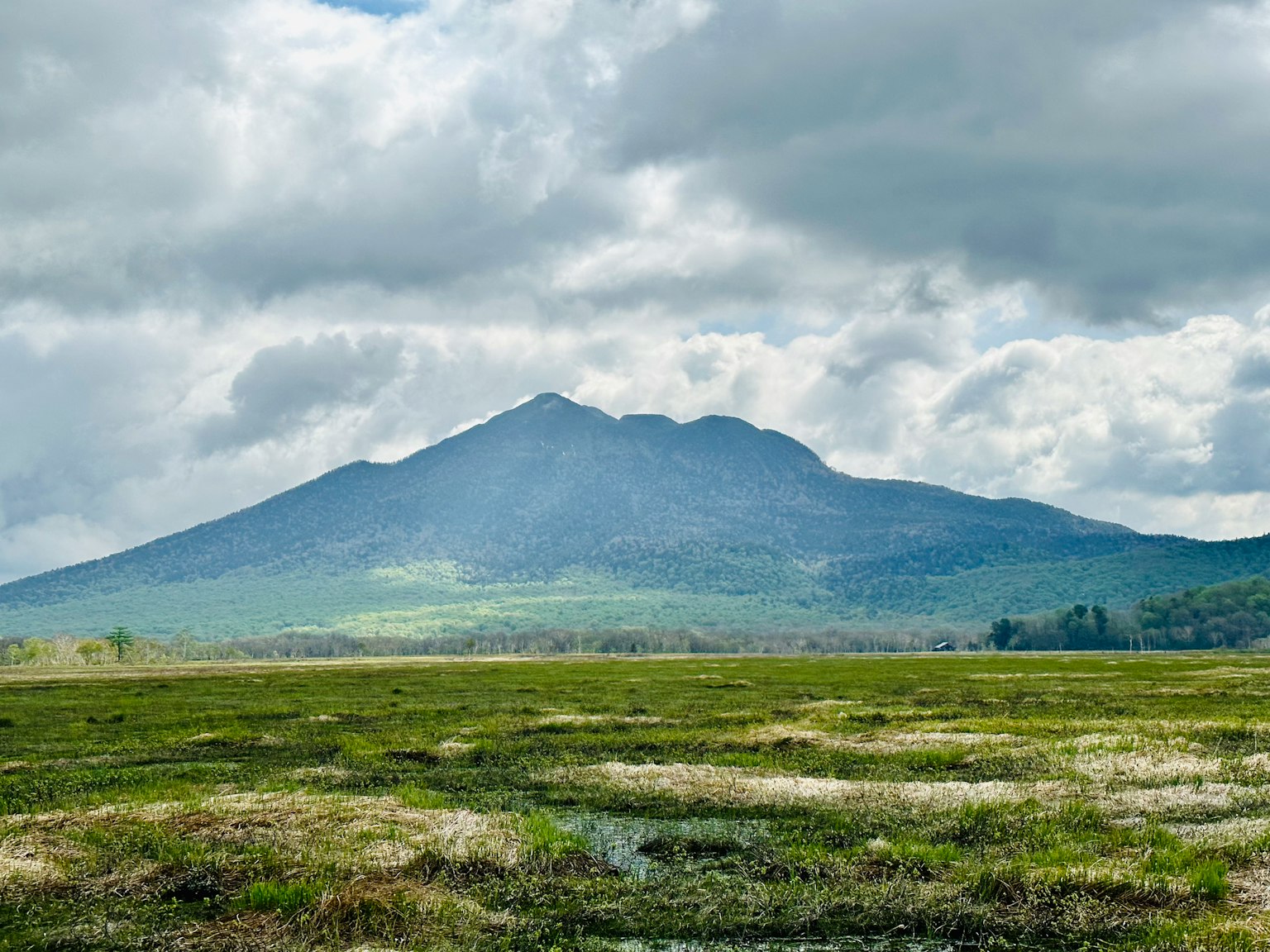 Vista escénica de una montaña rodeada de praderas verdes y nubes grises