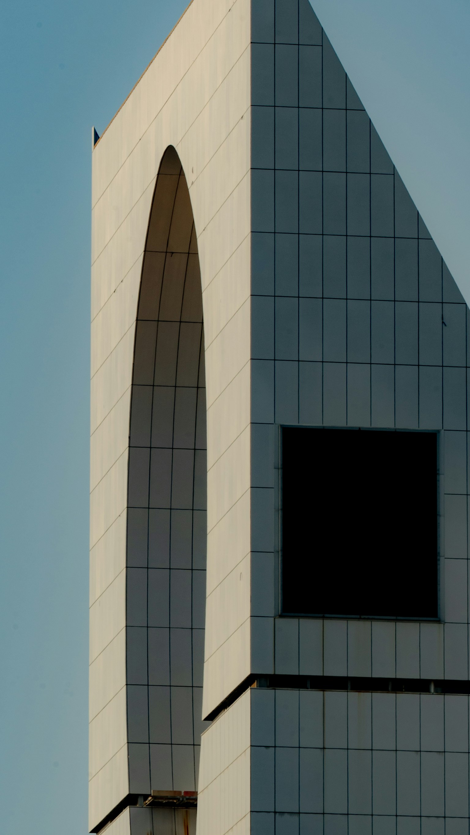 白いタイルで覆われた現代的な建物の一部 大きなアーチ型の窓と黒い正方形の窓が特徴