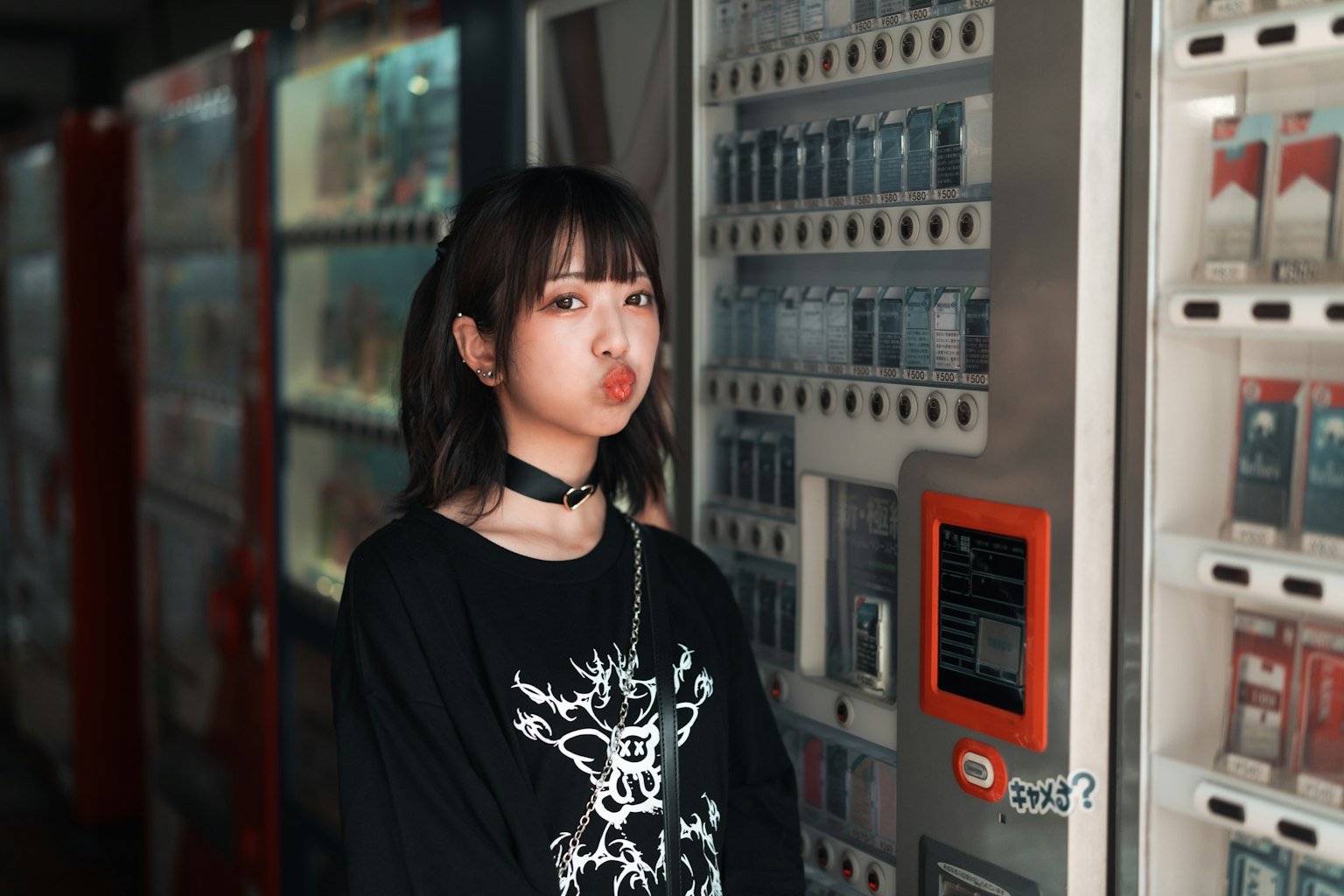 Ritratto di una donna davanti a distributori automatici che indossa una maglietta nera e un choker capelli alla lunghezza delle spalle