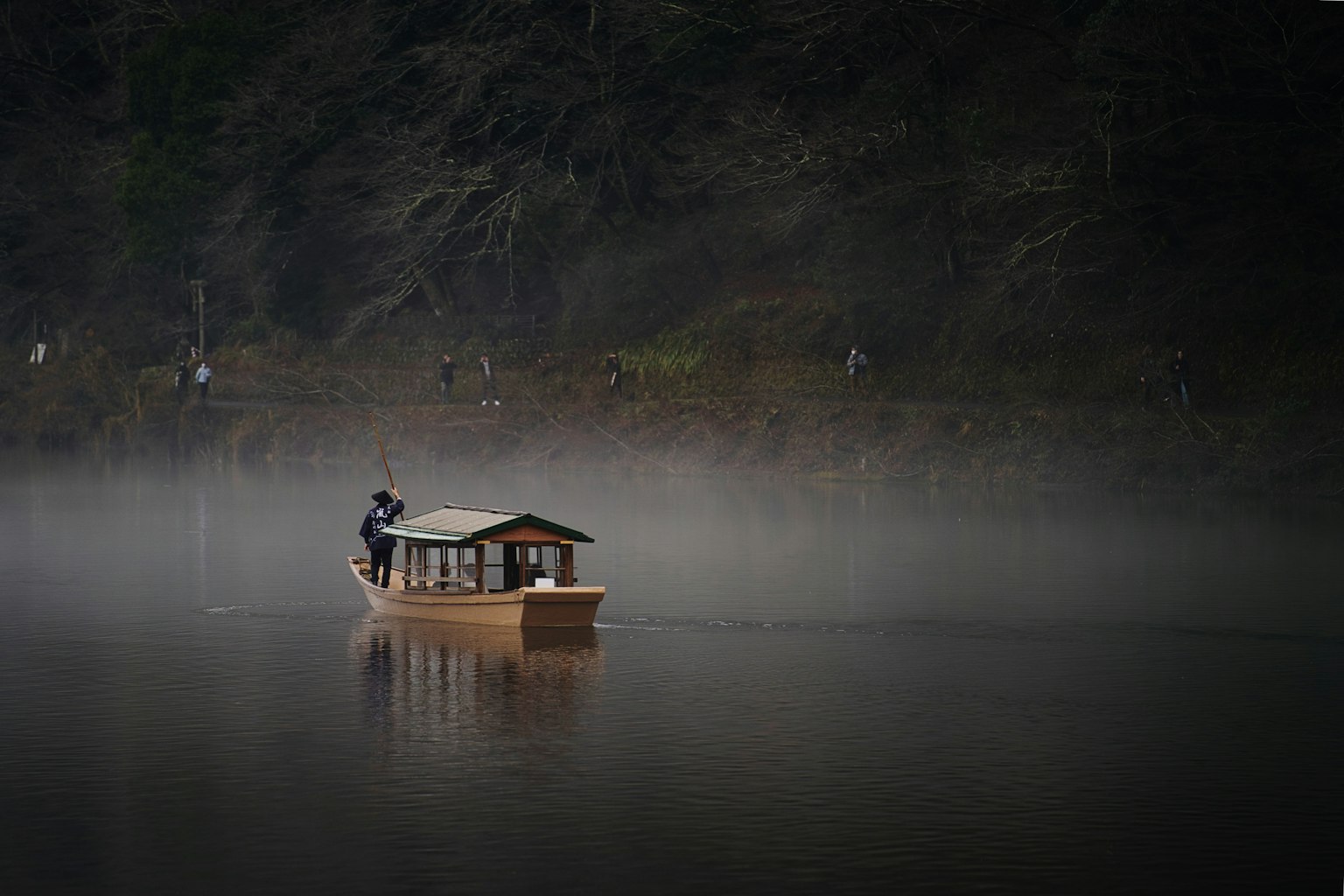 Un bateau en bois naviguant sur un lac brumeux avec une personne à bord