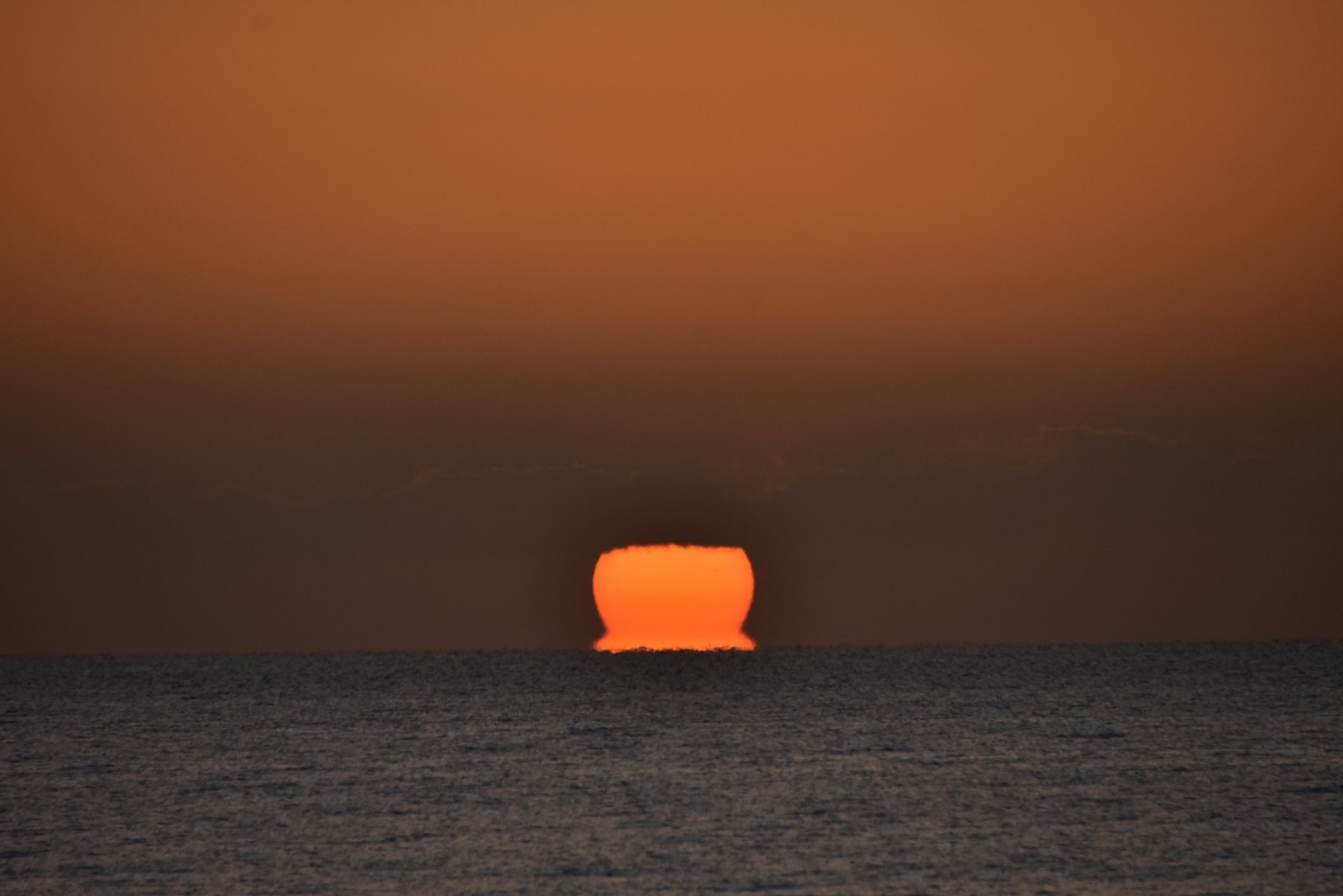 Grande sole arancione che tramonta all'orizzonte sopra l'oceano