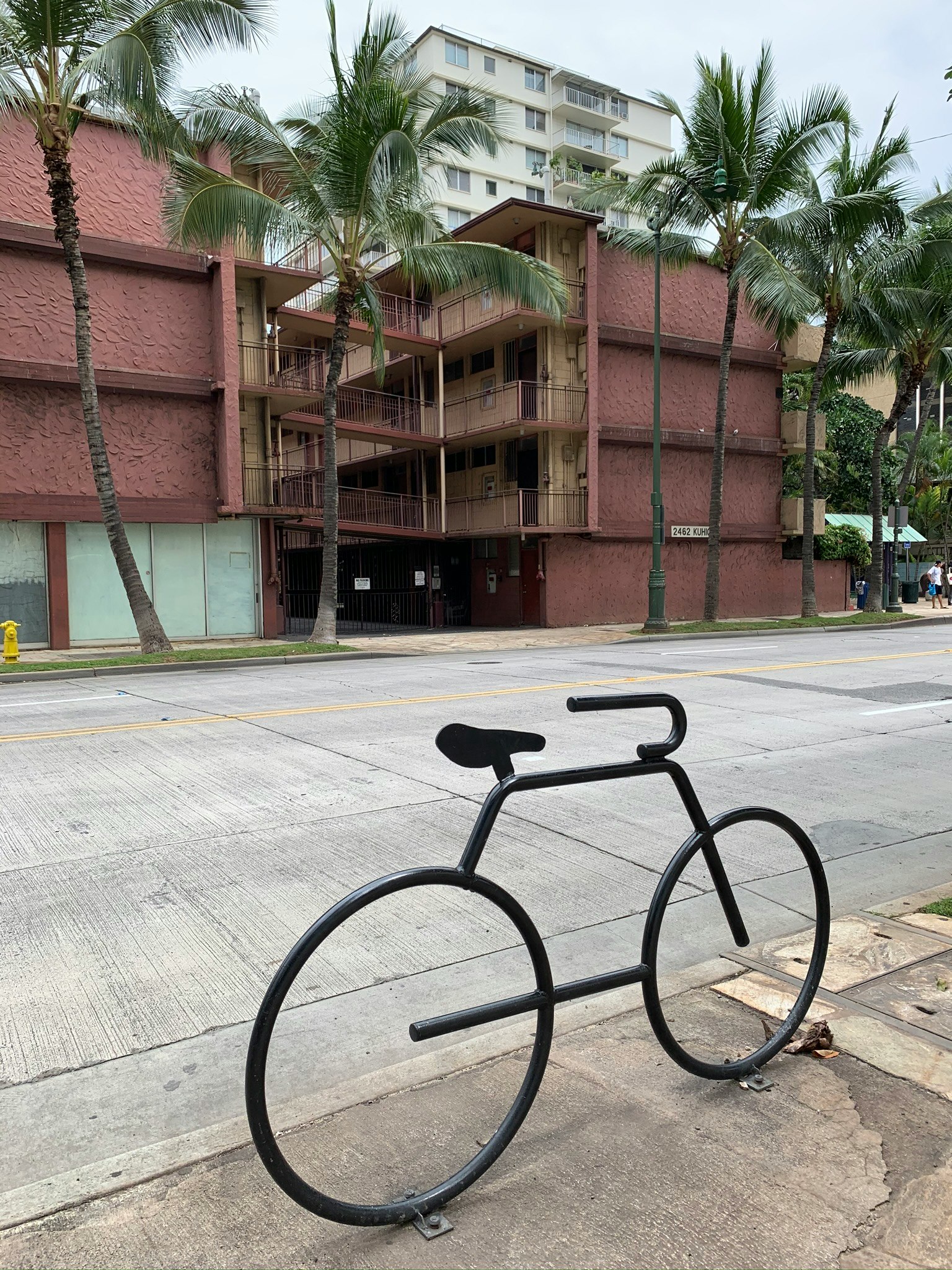 Schwarze Fahrradkunstinstallation auf der Straße mit Gebäude und Palmen im Hintergrund