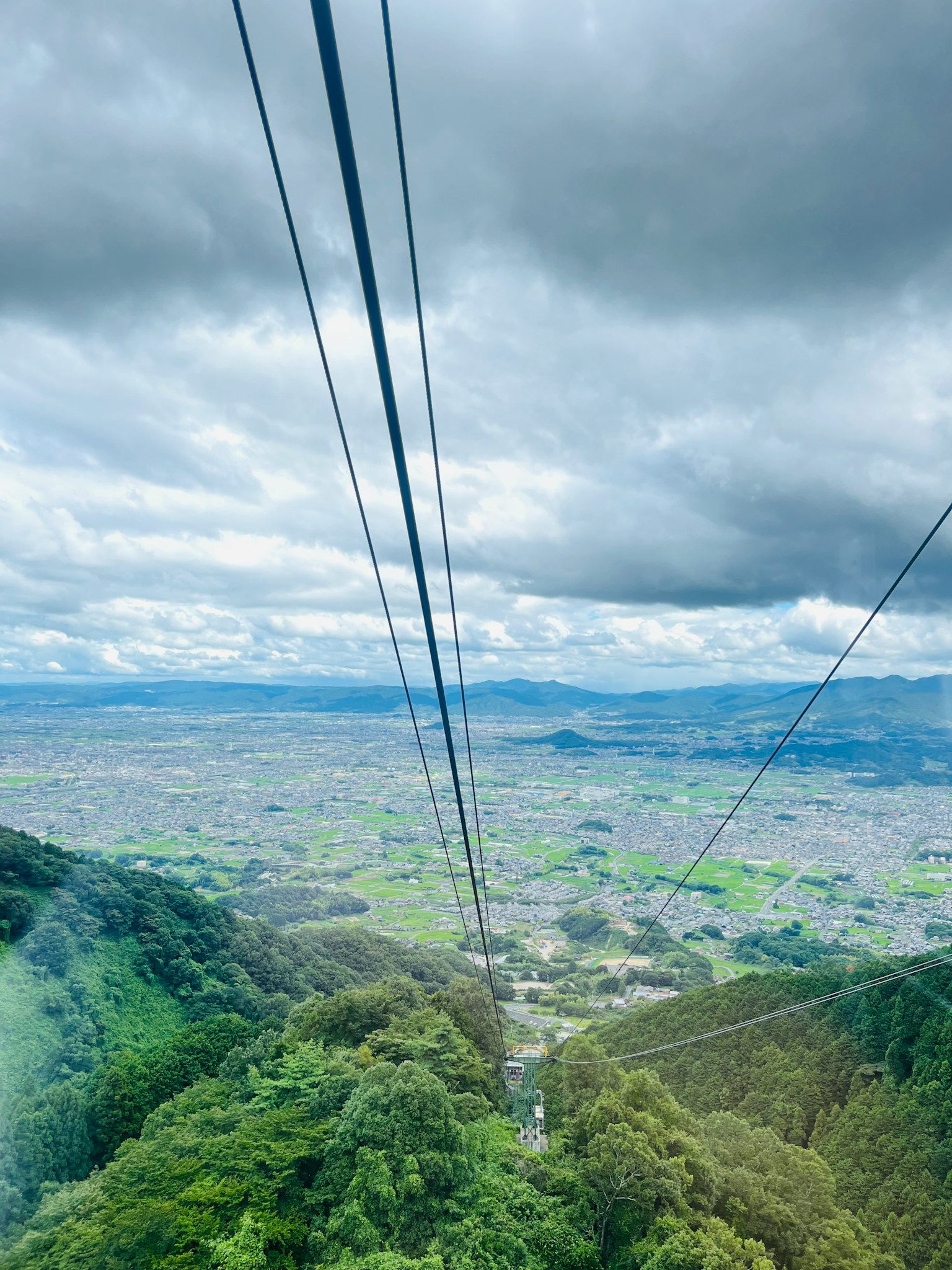 Vista da una funivia di montagna con vegetazione lussureggiante e cielo nuvoloso