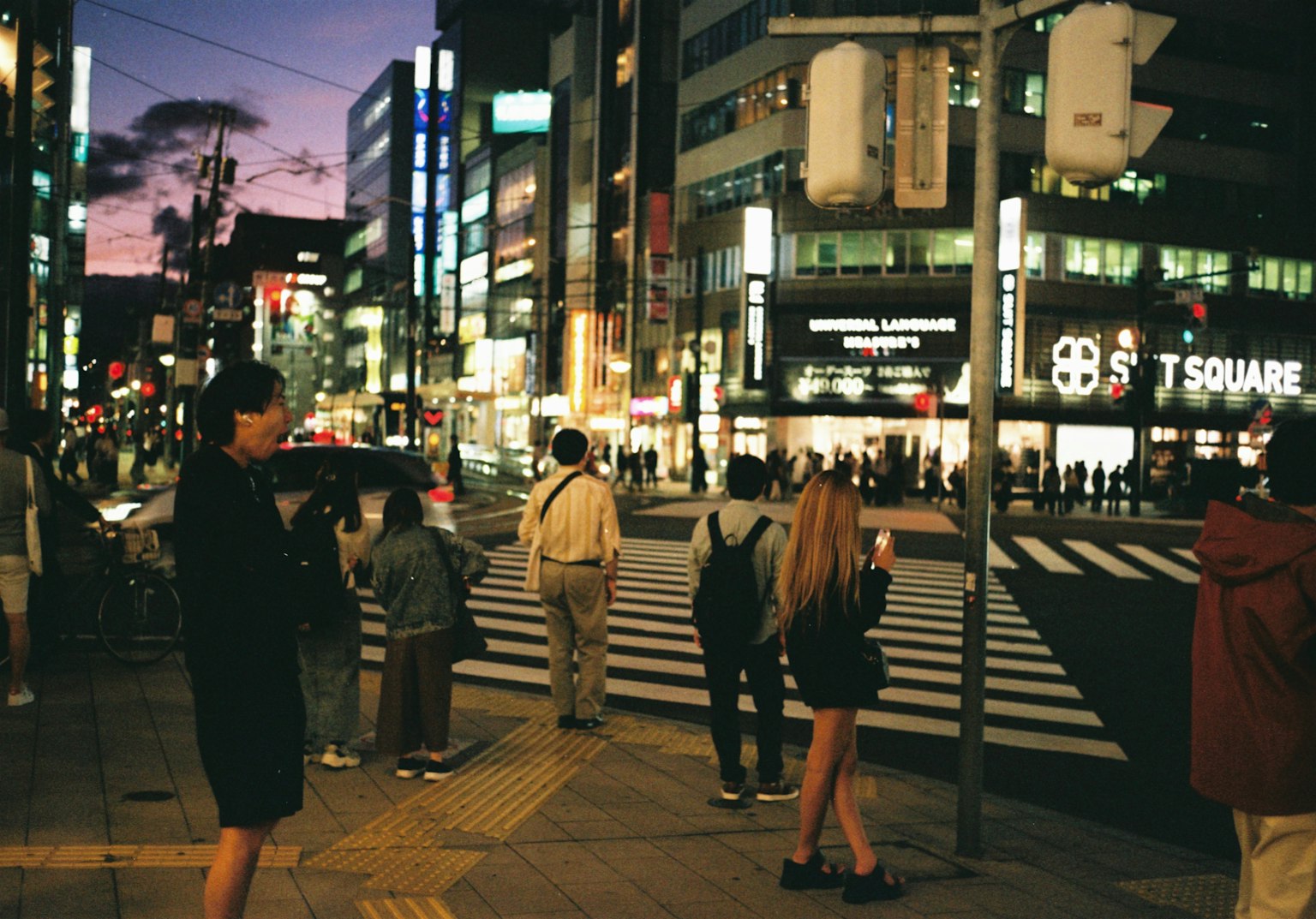 夕暮れ時の繁華街で横断歩道を待つ人々とビルの明かり