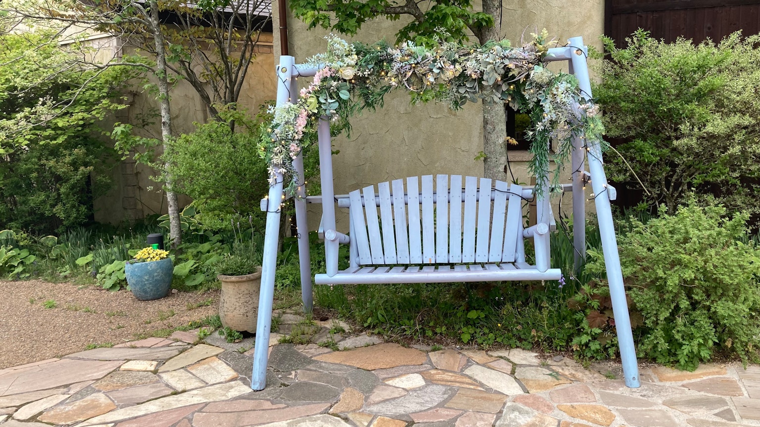Une balançoire bleue entourée de plantes vertes dans un jardin