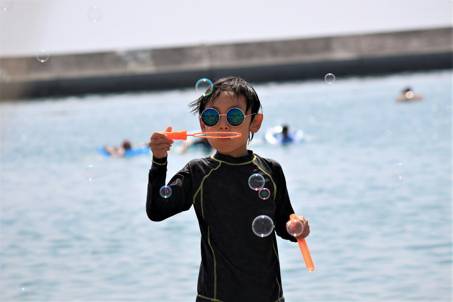 水辺で泡を作る子供 黒いウェットスーツとサングラスを着用