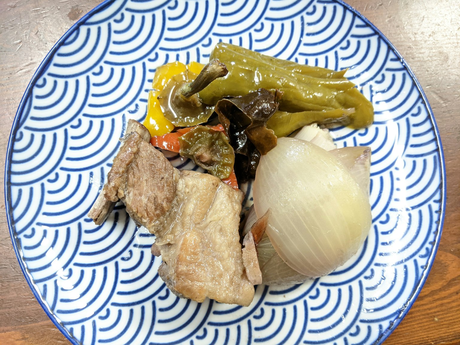 Un piatto di carne e verdure servito su un piatto a motivi ondulati blu