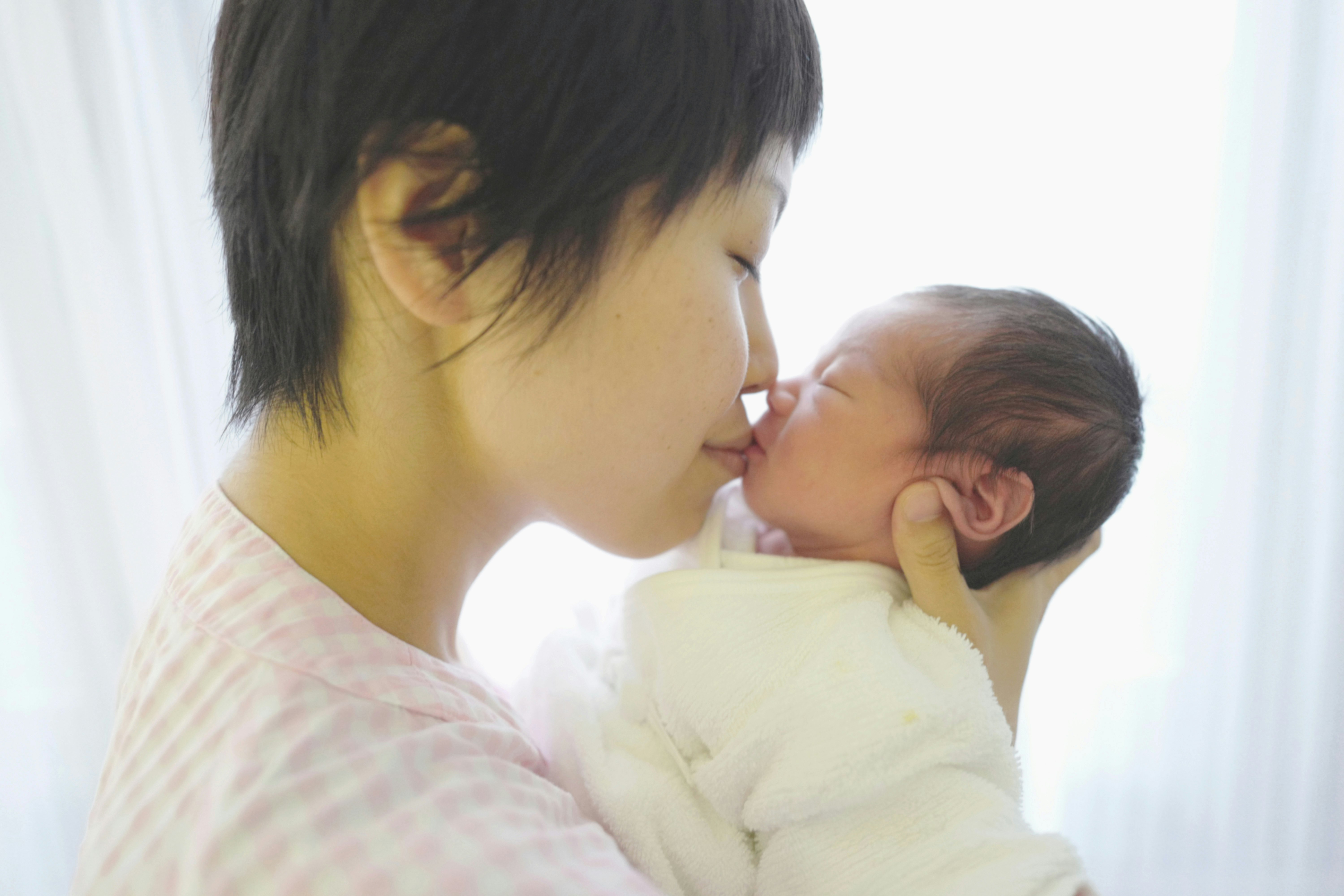 赤ちゃんを抱いてキスする母親と新生児の親子の瞬間