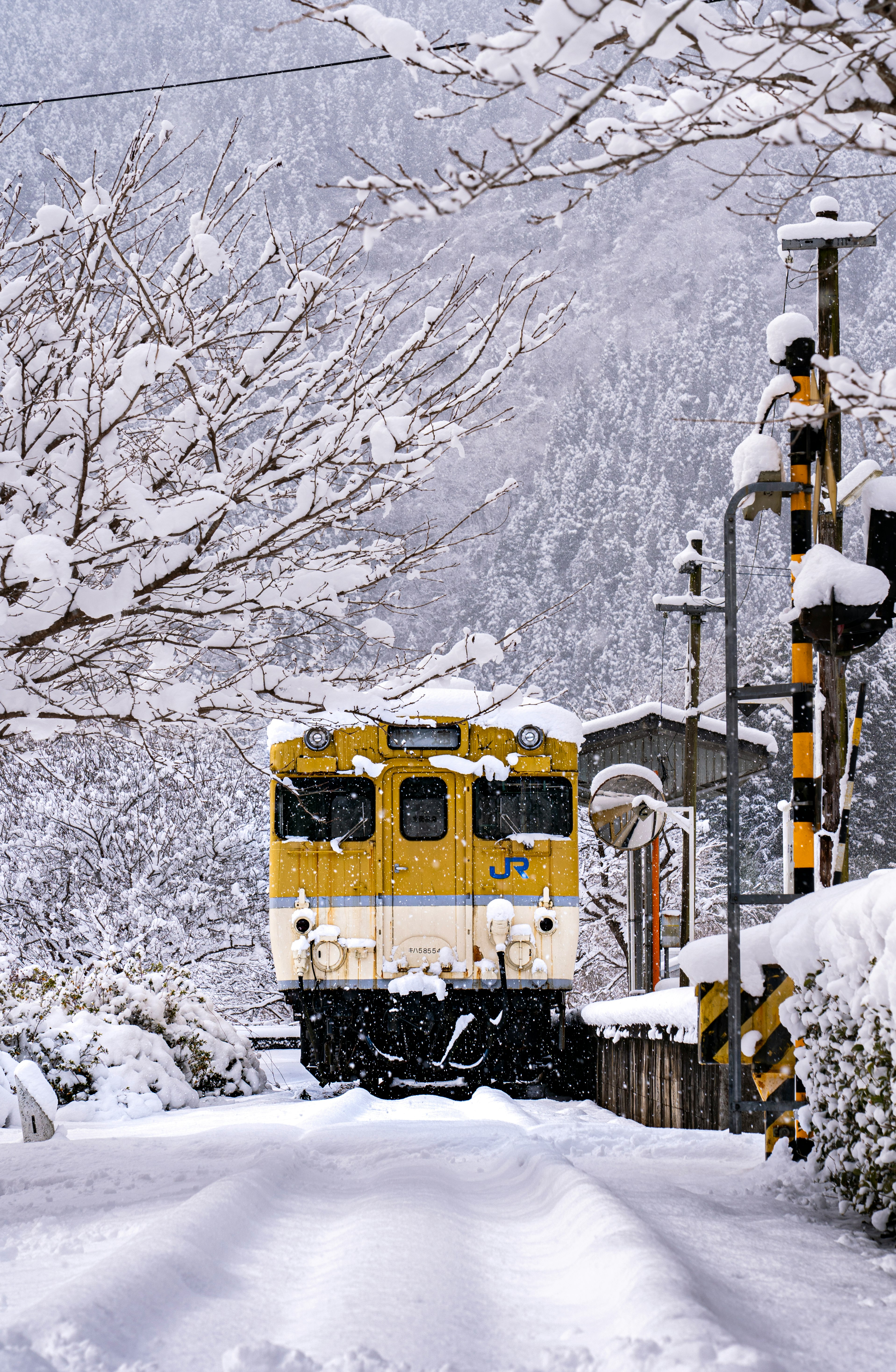 雪景色の踏切と黄色い列車が走る冬の街並み