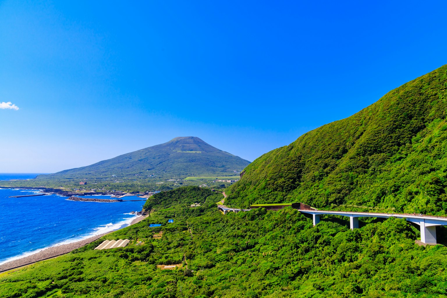Scenic view of lush green mountains along a blue ocean with a winding road