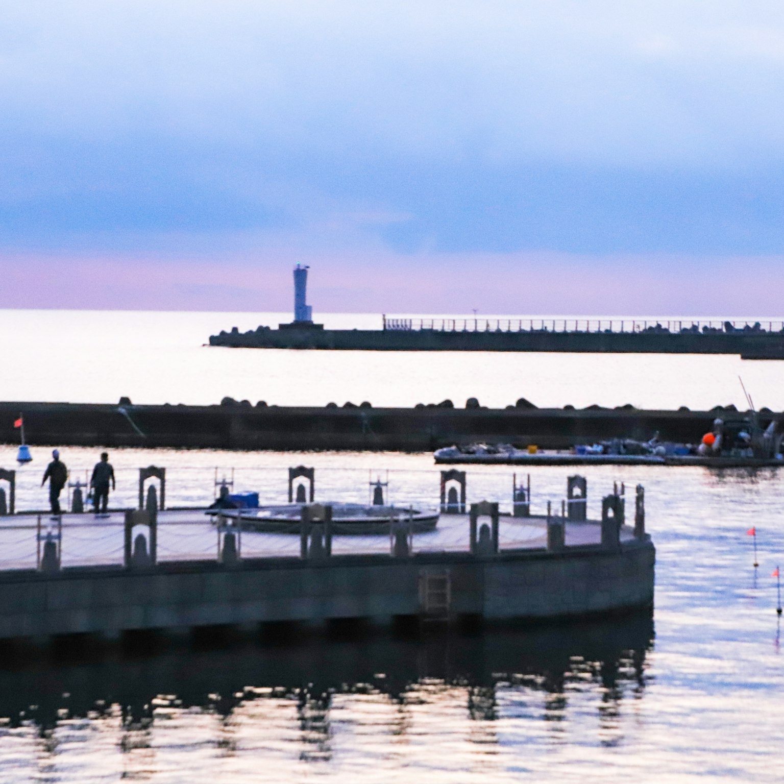 Paisaje marino sereno con personas caminando en un muelle y un faro a lo lejos