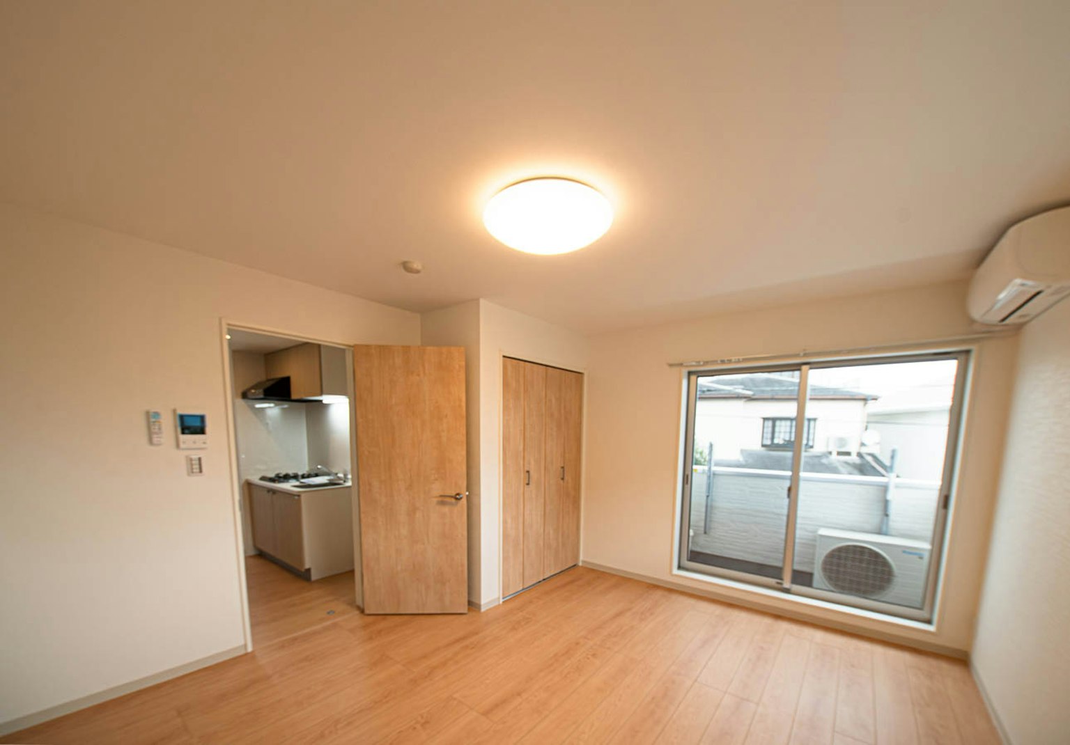 Bright and simple interior with cream walls and wooden flooring door to kitchen and window