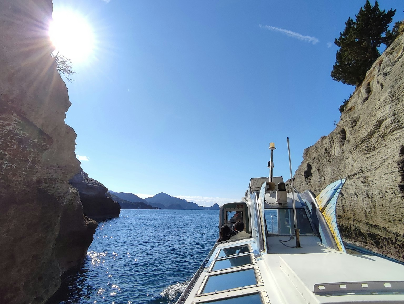 Boat navigating between cliffs under a bright sun