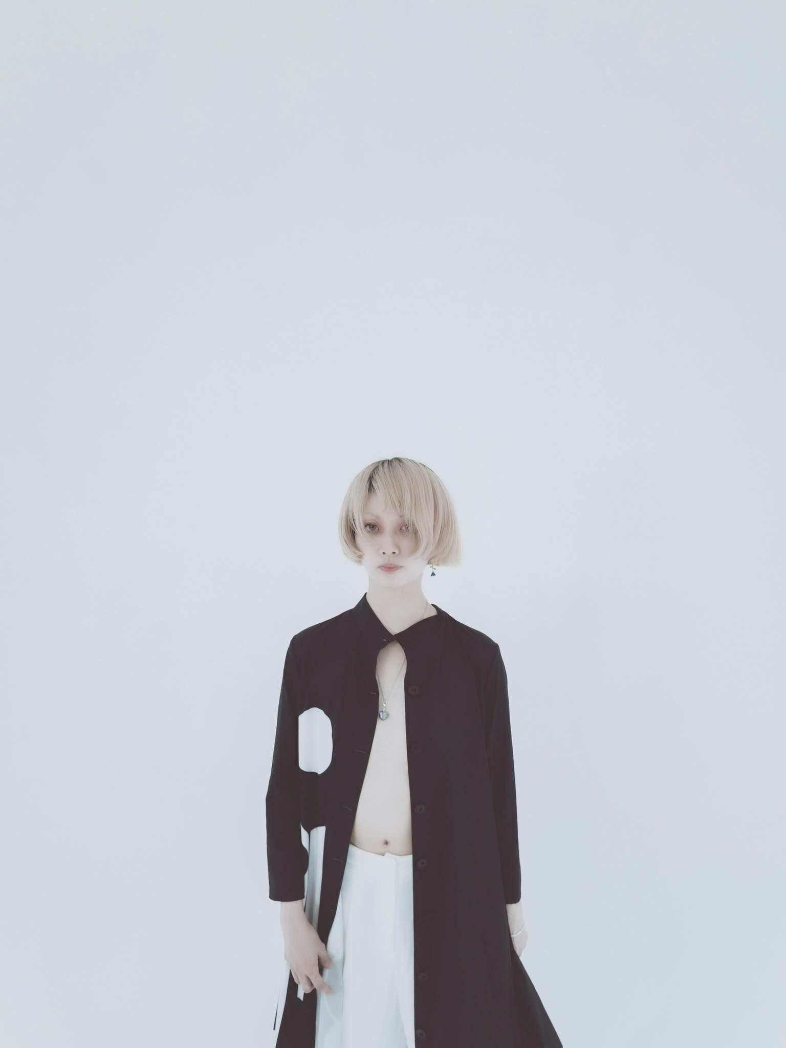 白い背景の前に立つ金髪のモデル 黒いコートを着ている