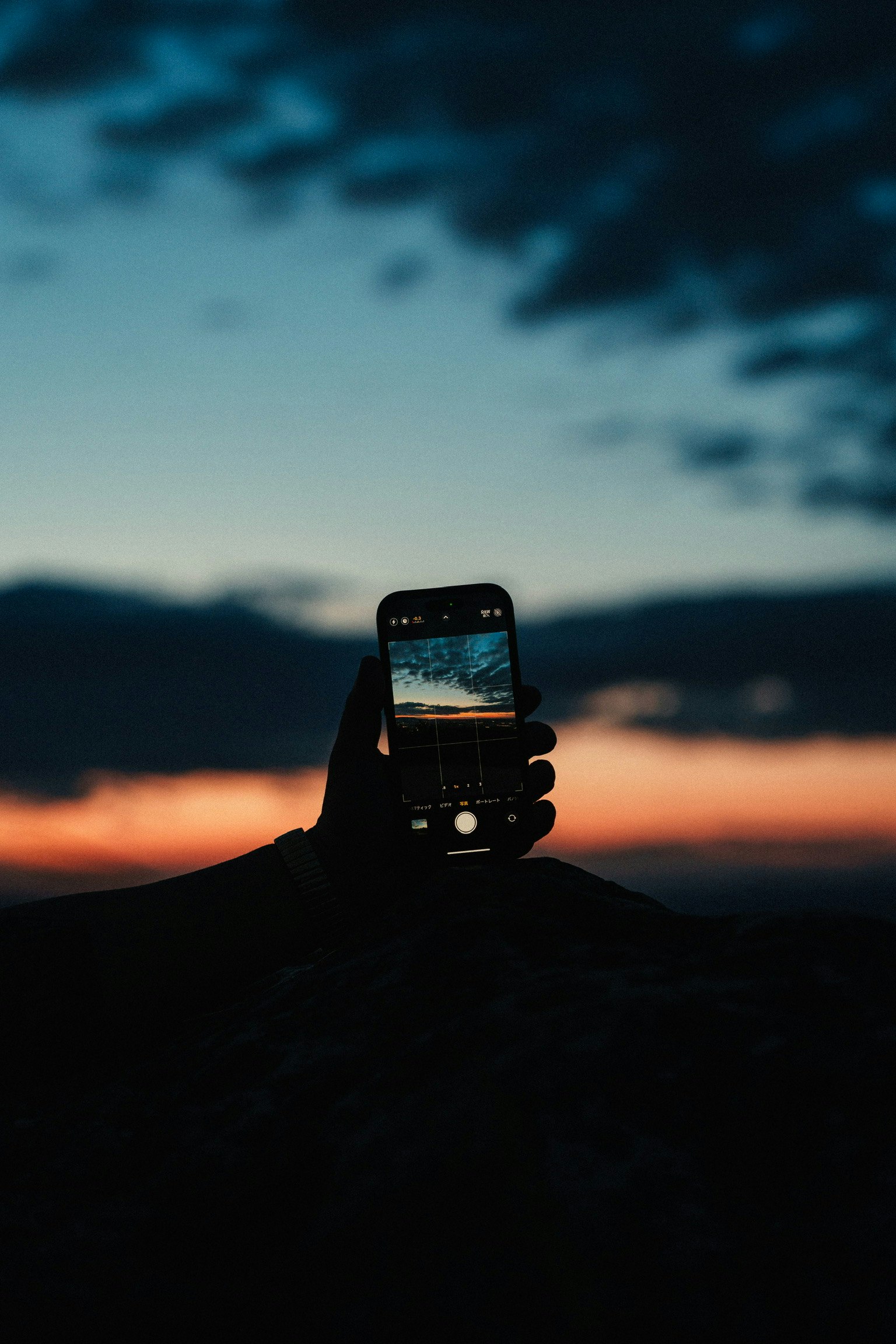Siluet tangan memegang smartphone di latar belakang langit senja