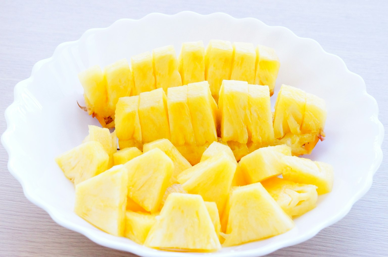 Lebensmittelbild mit geschnittenem, leuchtend gelbem Ananas in einer weißen Schüssel