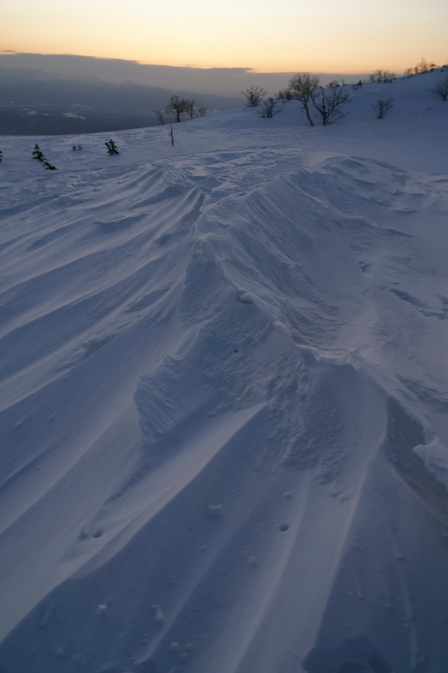 Snow-covered terrain with wave-like patterns and sunset light