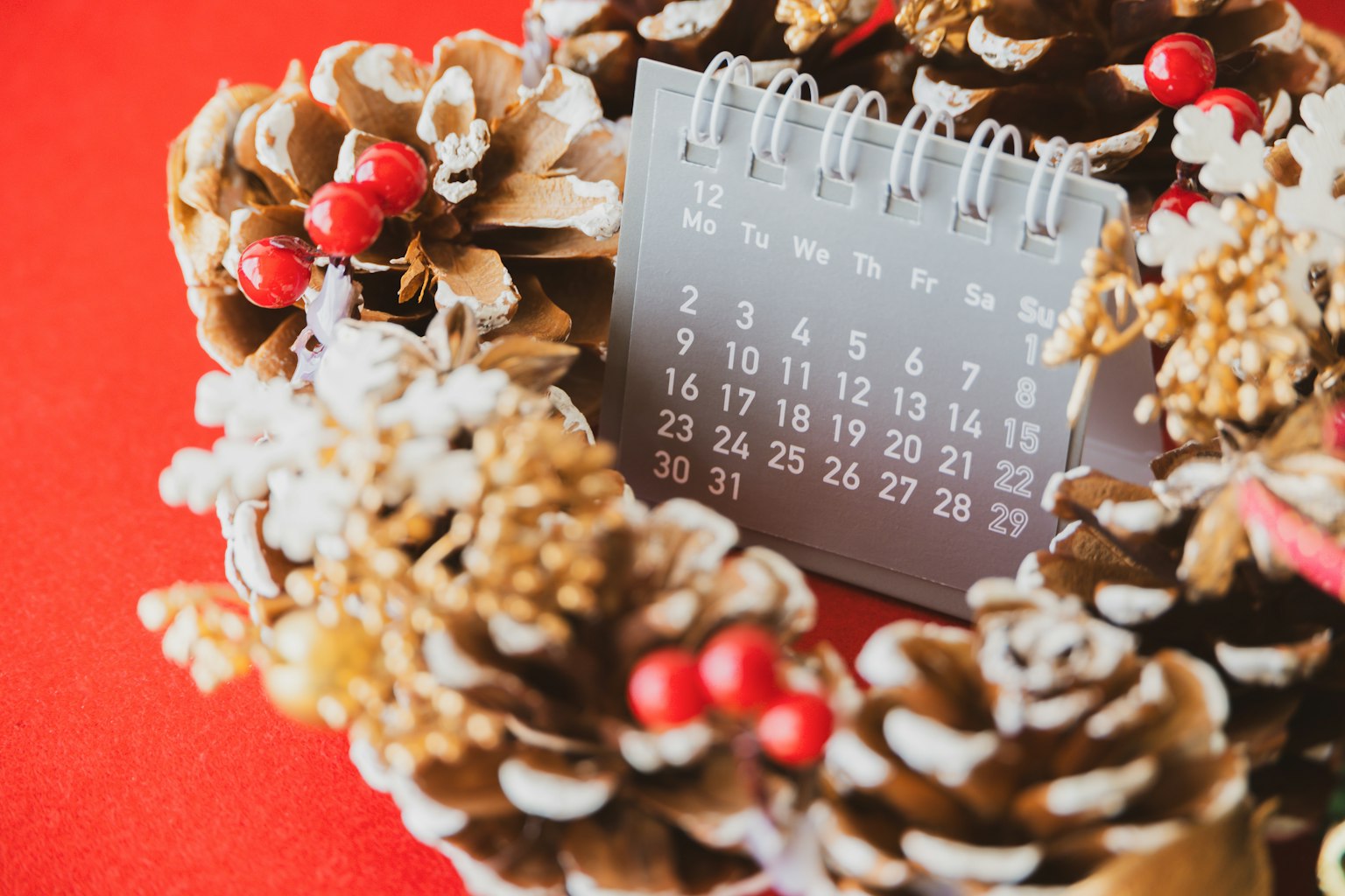 Un calendario posizionato all'interno di una corona di Natale realizzata con pigne e bacche rosse