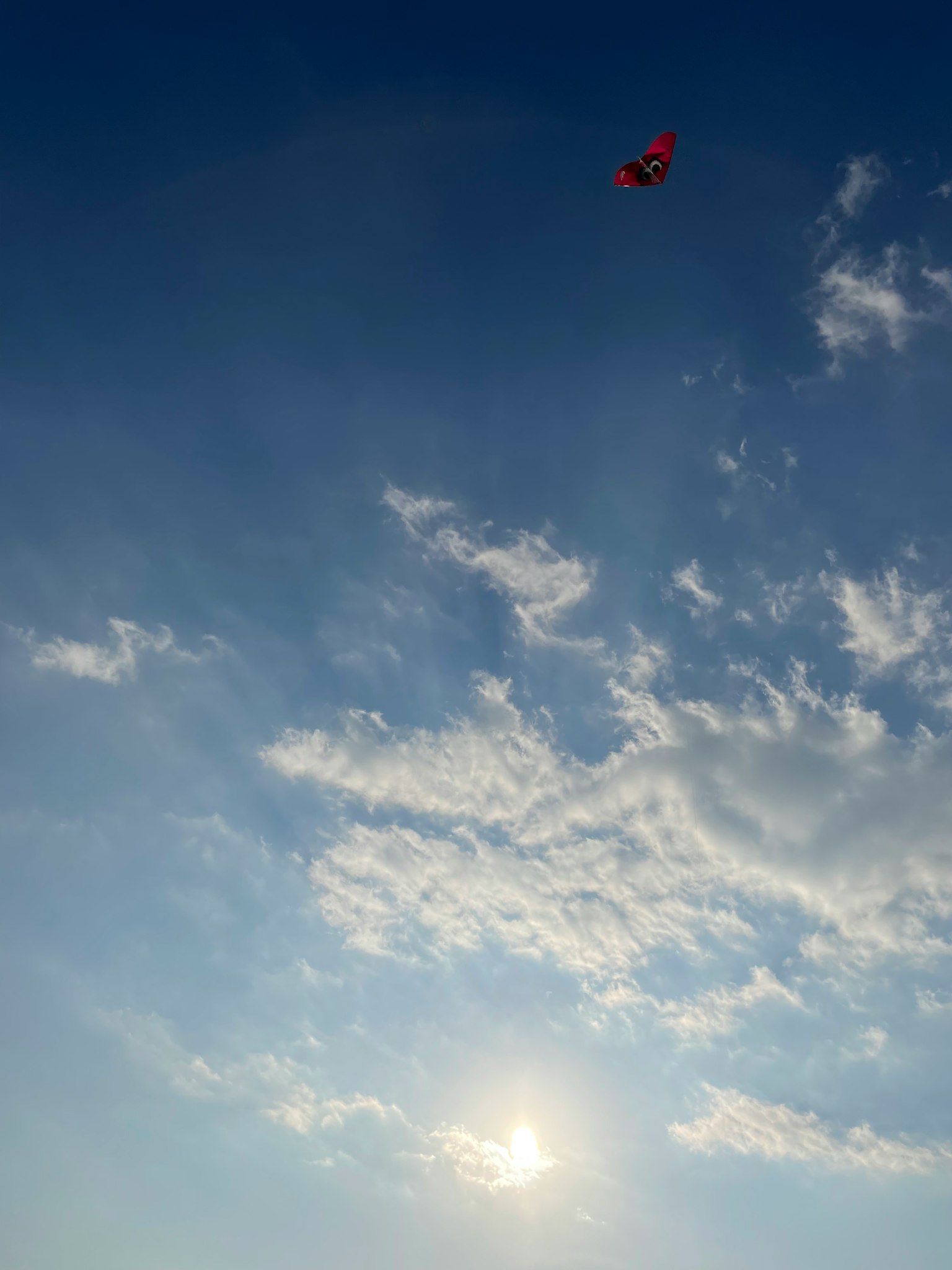 Ein roter Drachen fliegt in einem blauen Himmel mit verstreuten Wolken