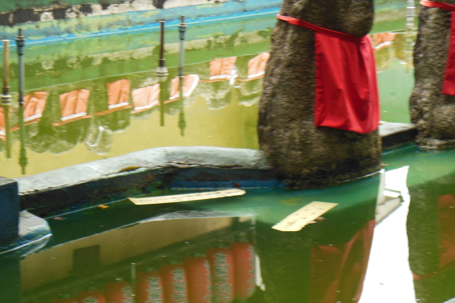 Statue di pietra coperte di tessuto rosso riflesse nell'acqua verde