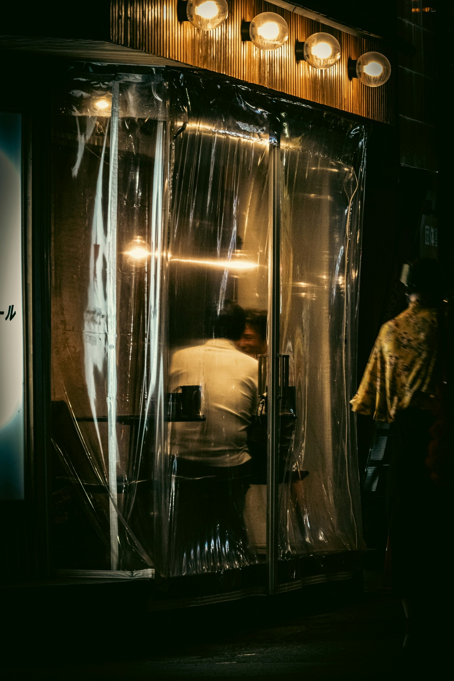 一个人坐在一个昏暗的商店里，外面覆盖着塑料膜
