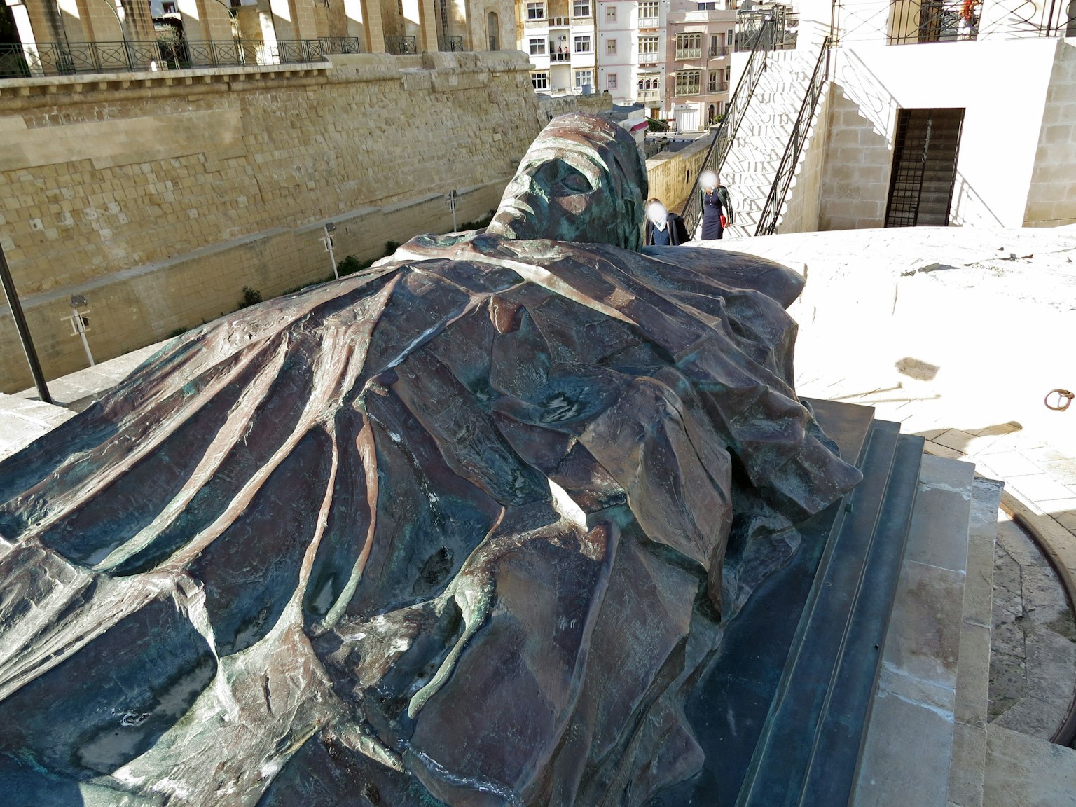 Une sculpture en bronze d'une figure allongée avec des textures visibles et des personnes en arrière-plan