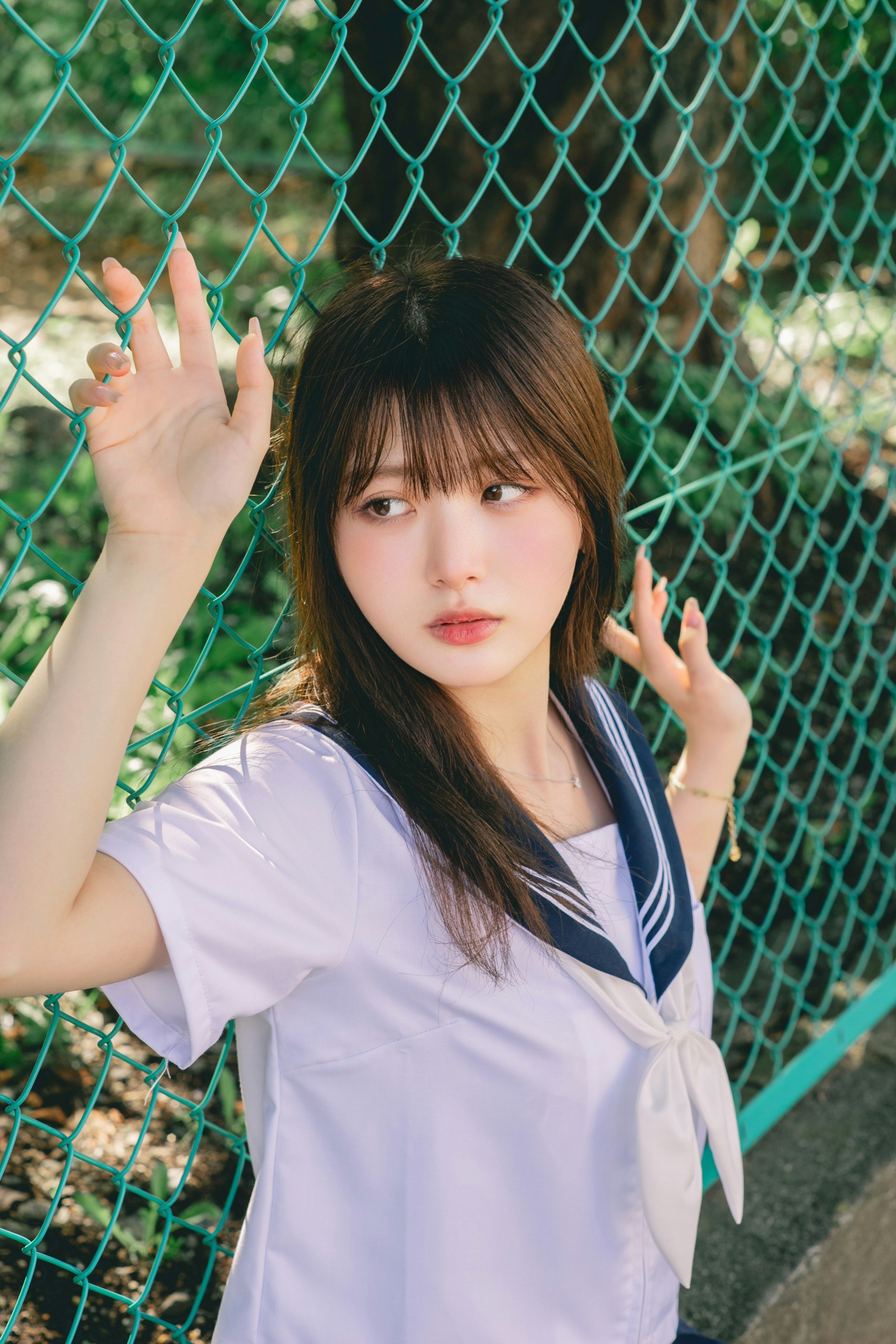 Woman in a school uniform posing behind a fence