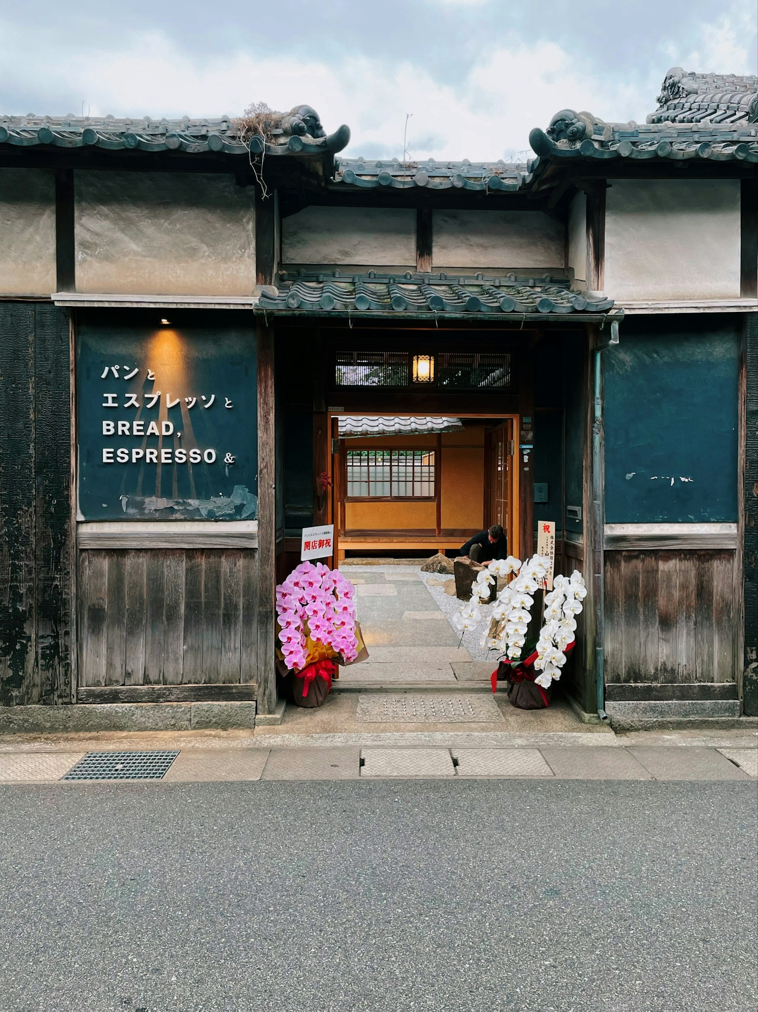 Entrance of a traditional Japanese building with a sign for espresso and bread adorned with colorful flowers