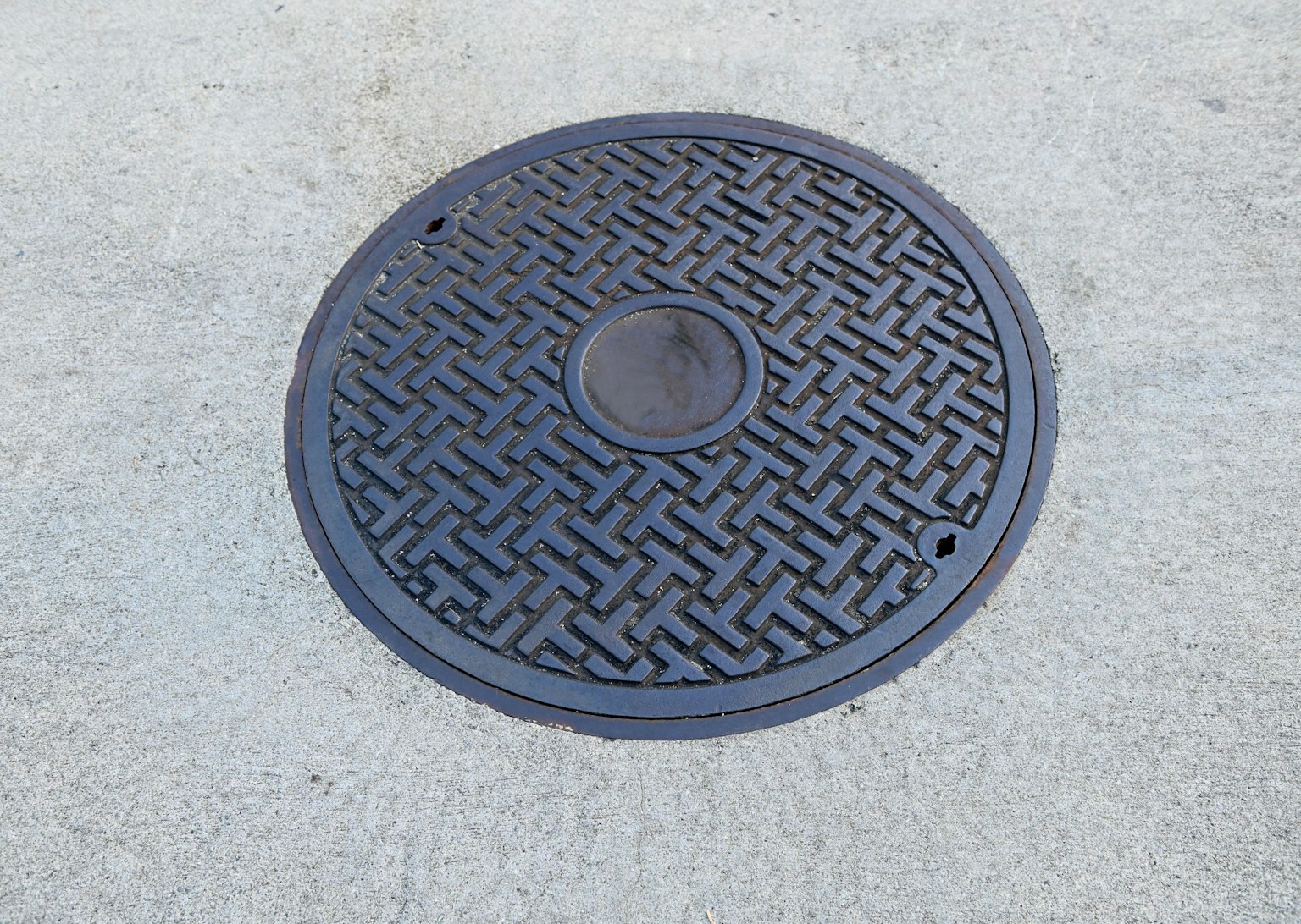 Schwarzer Kanaldeckel mit geometrischem Muster
