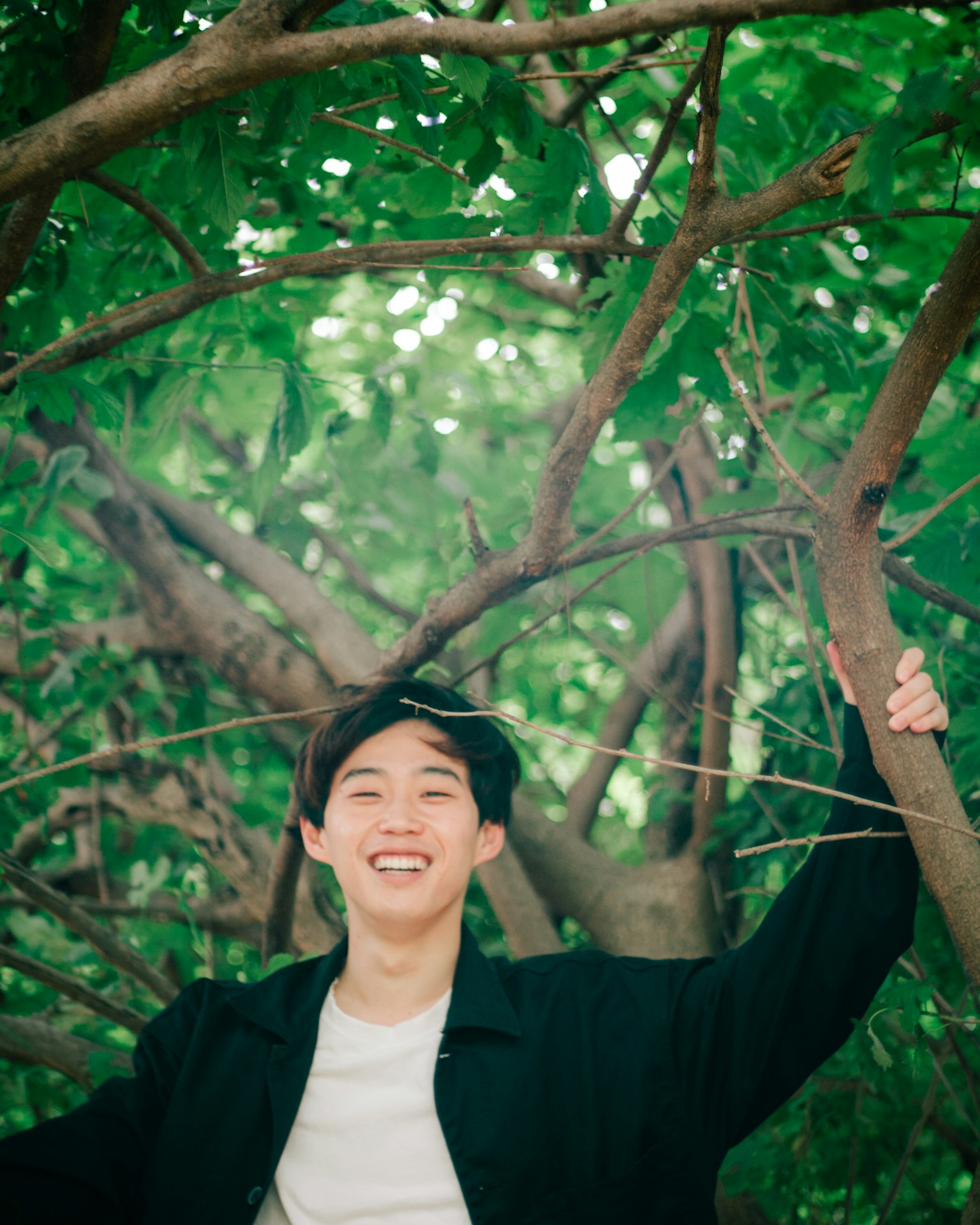 ชายหนุ่มยิ้มอย่างมีความสุขท่ามกลางต้นไม้สีเขียว