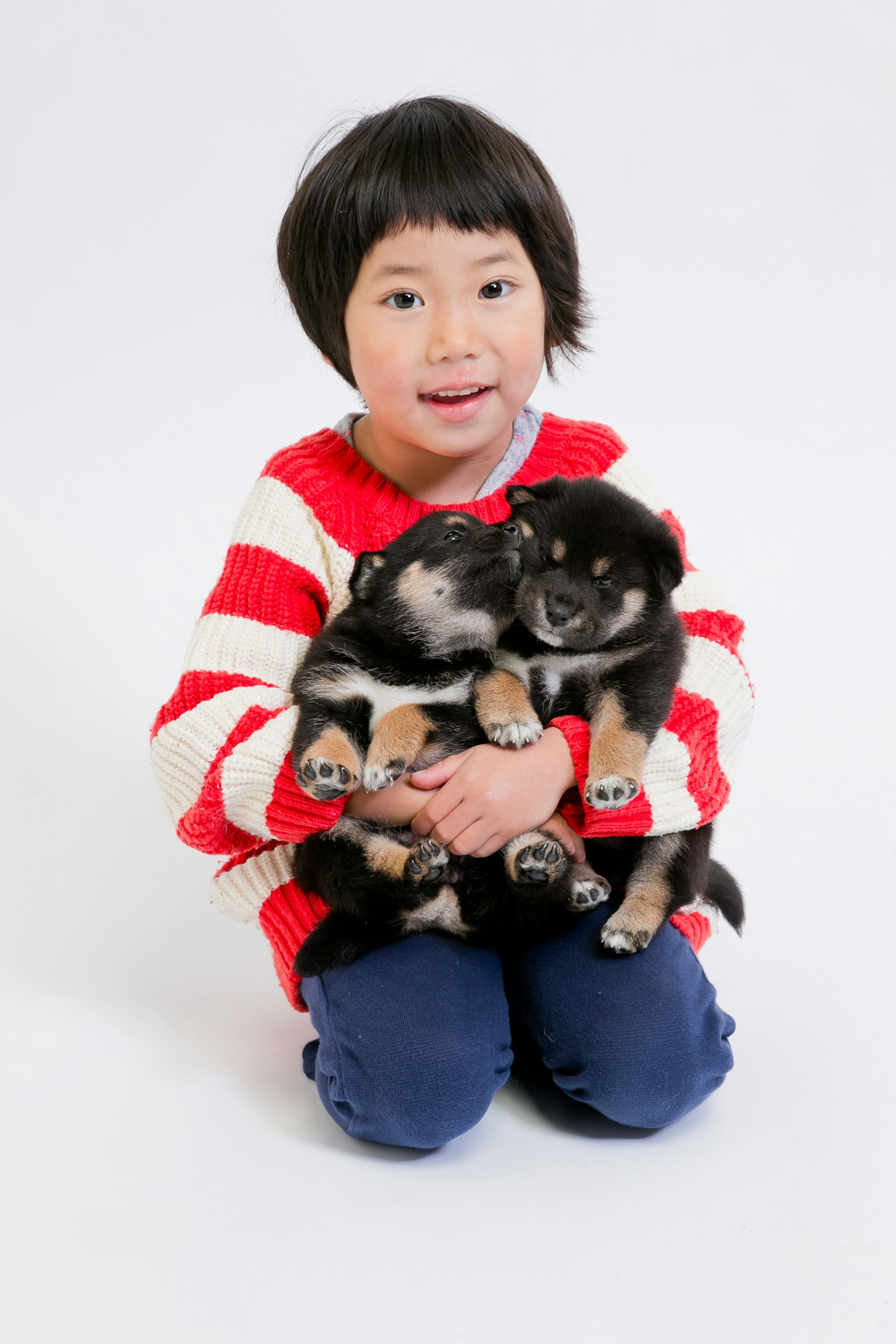 Seorang anak dengan sweter bergaris merah memegang dua anak anjing