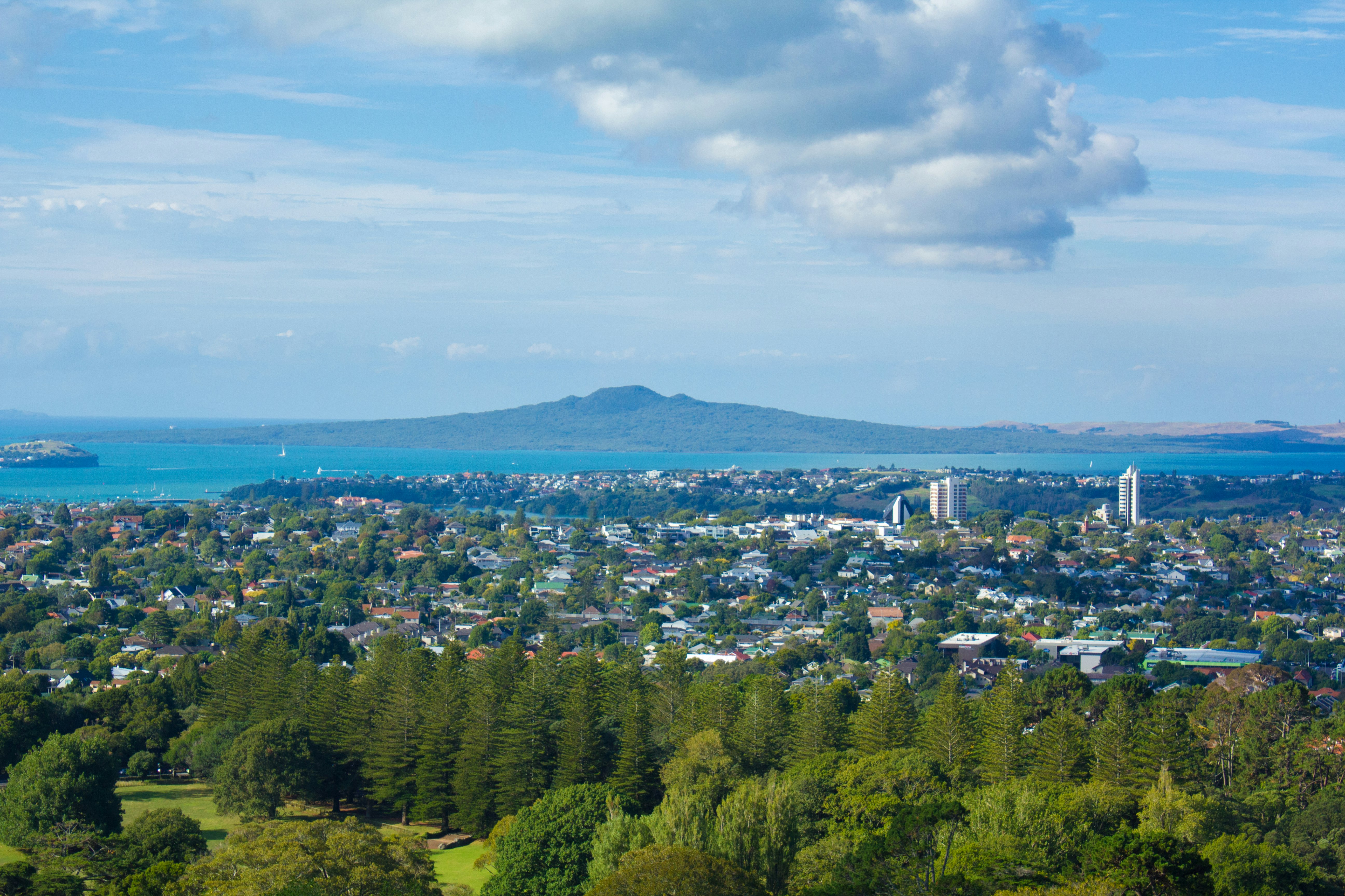 Blick auf das Meer und die Stadt von grünen Hügeln mit fernen Bergen