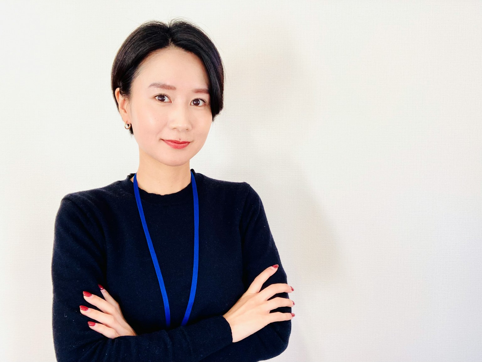 A woman in a black sweater standing with arms crossed in front of a simple background